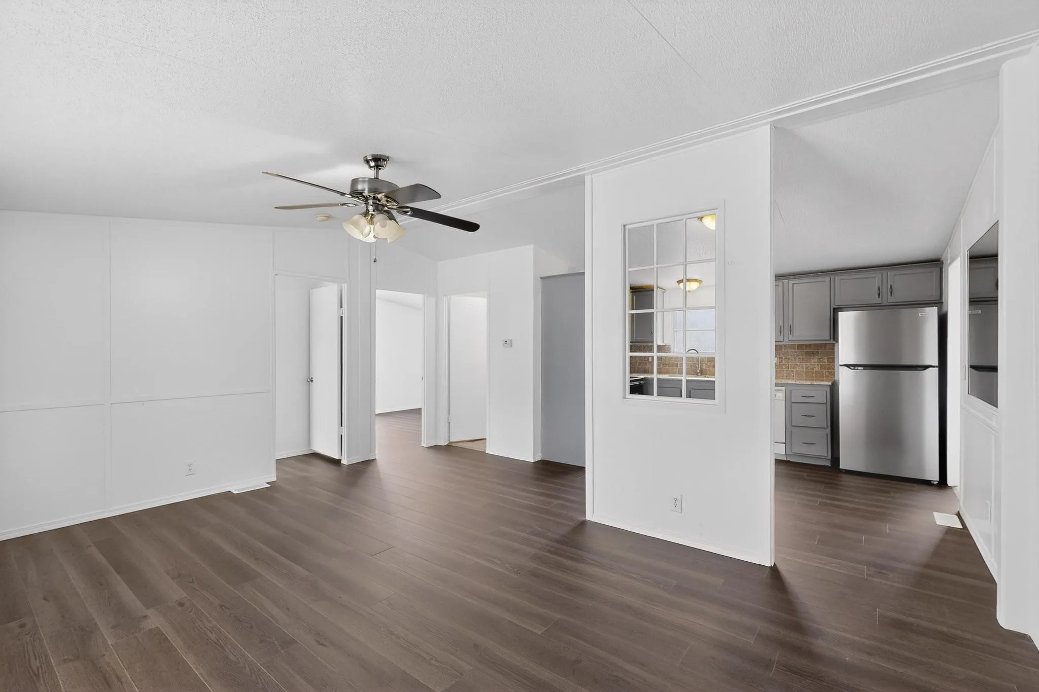 Unfurnished living room with a ceiling fan, dark wood-style floors, and a textured ceiling