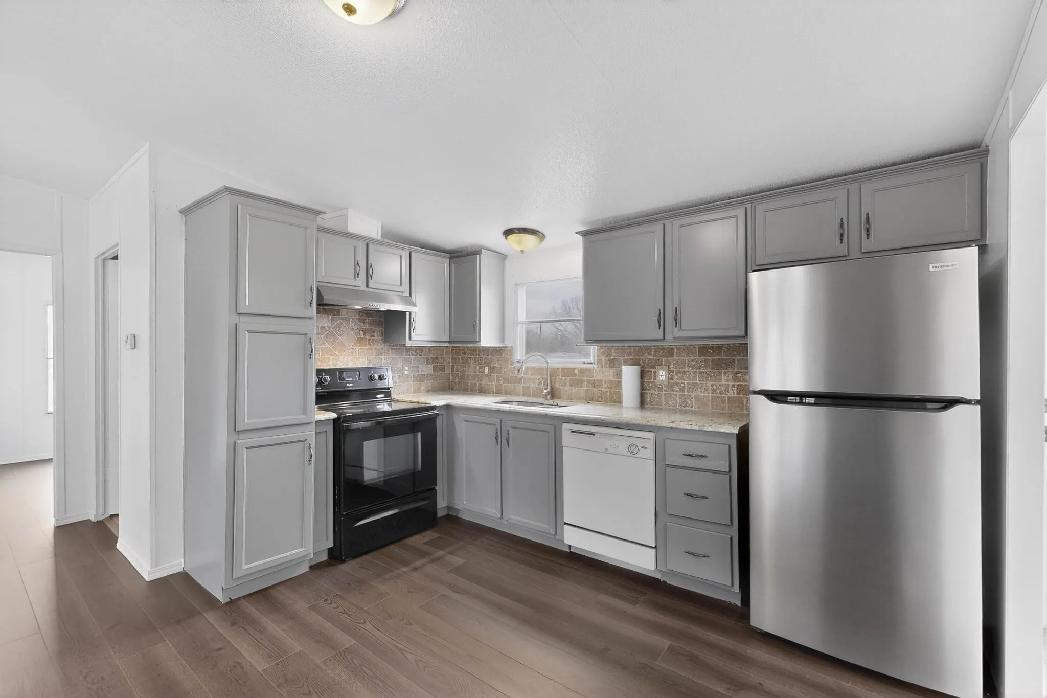 Kitchen featuring freestanding refrigerator, black / electric stove, dark wood-type flooring, dishwasher, and gray cabinetry