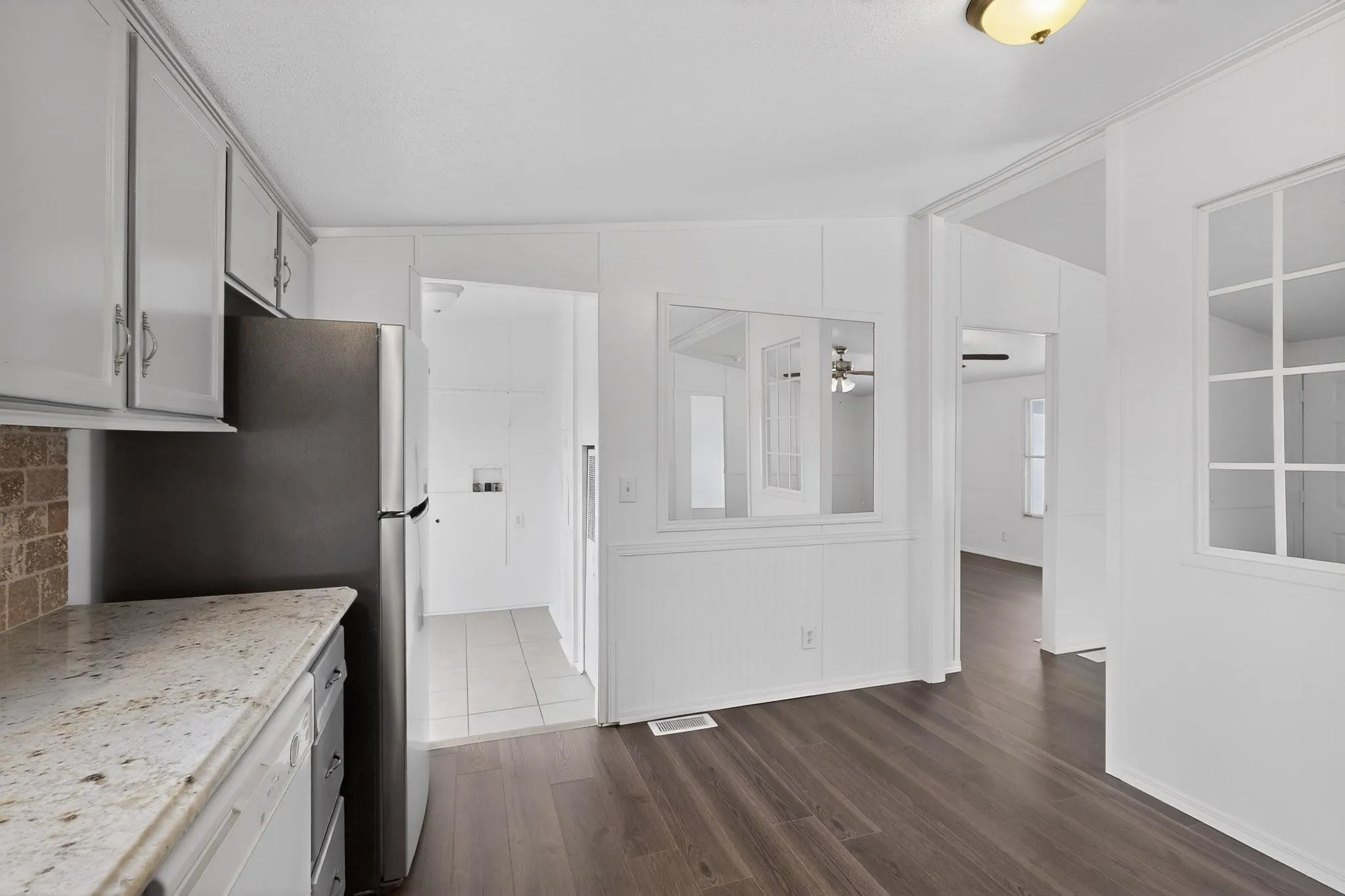 Kitchen featuring dark wood-style flooring, dishwasher, lofted ceiling, freestanding refrigerator, and light stone countertops