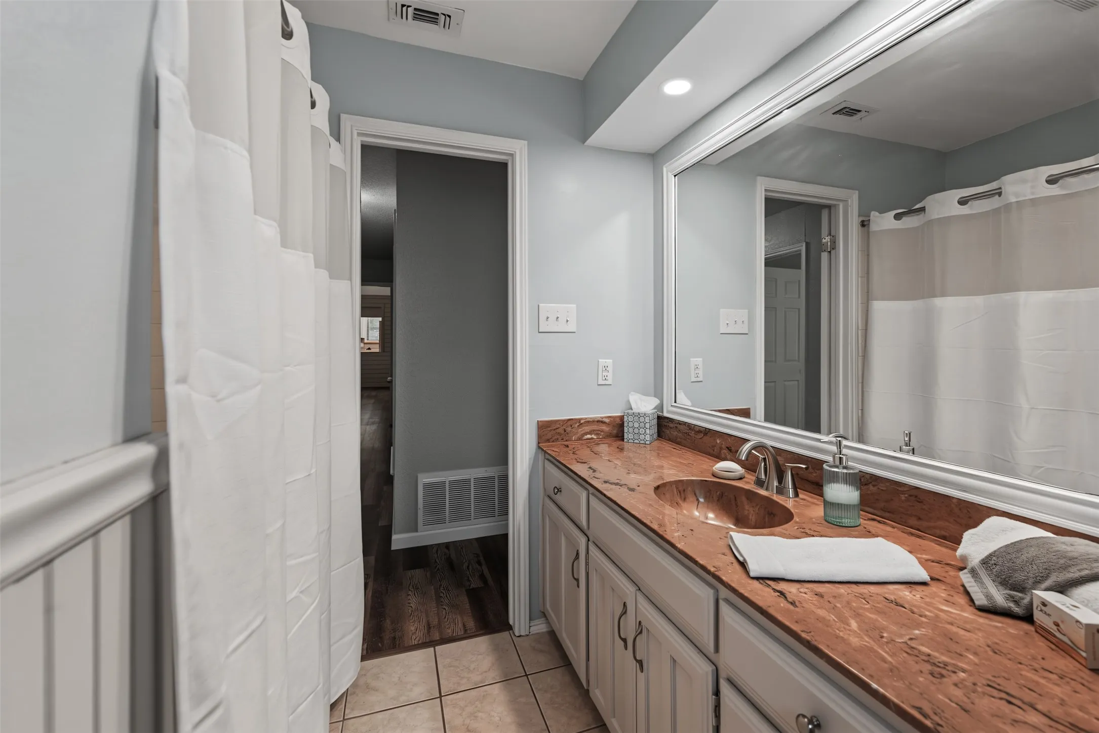 Guest bath: Vanity with an integrated single basin, expansive mirror, cabinetry, and tiled flooring