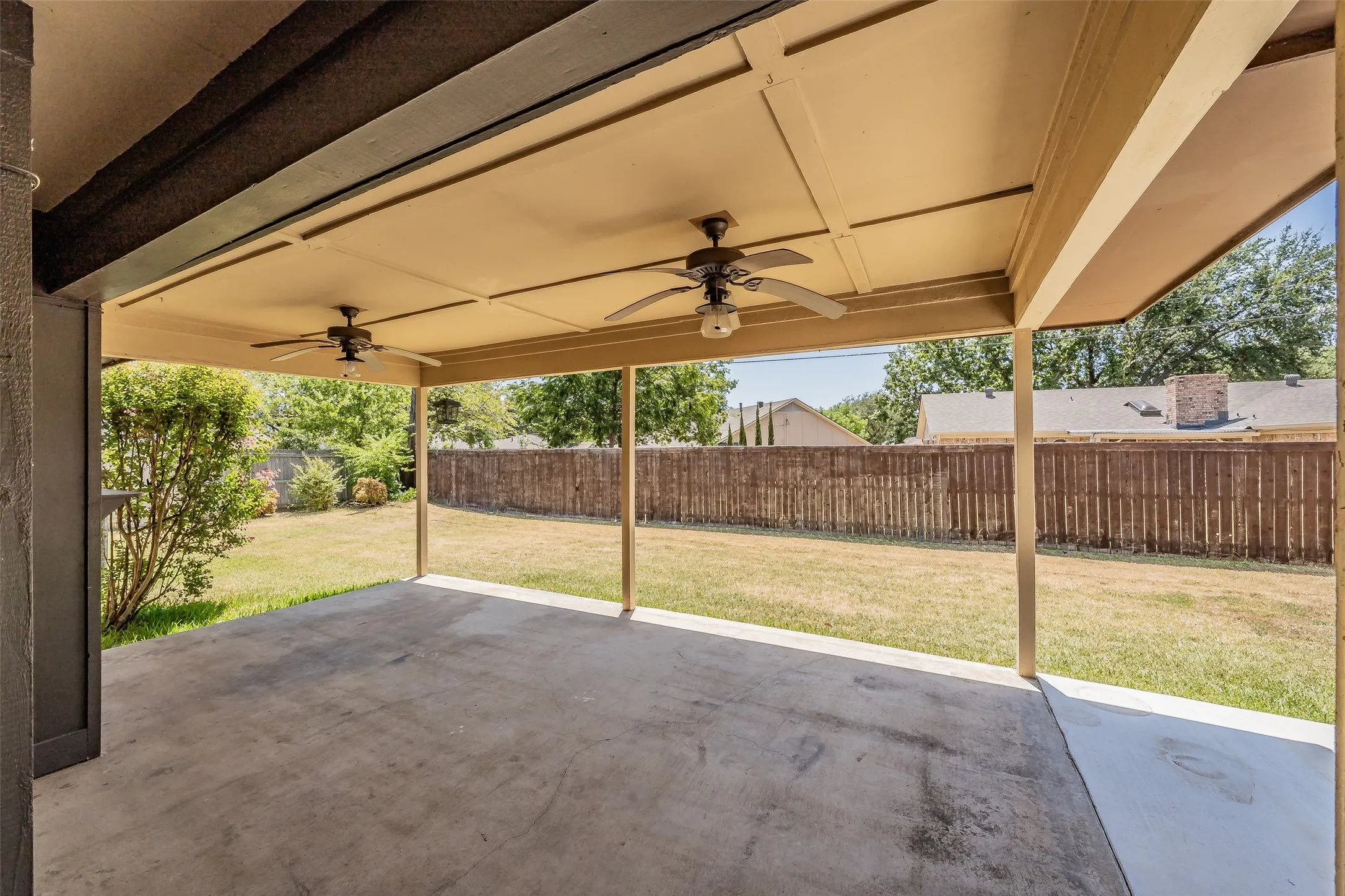 Covered patio with a concrete slab, two ceiling fans, and a spacious grassy yard featuring a wood fence