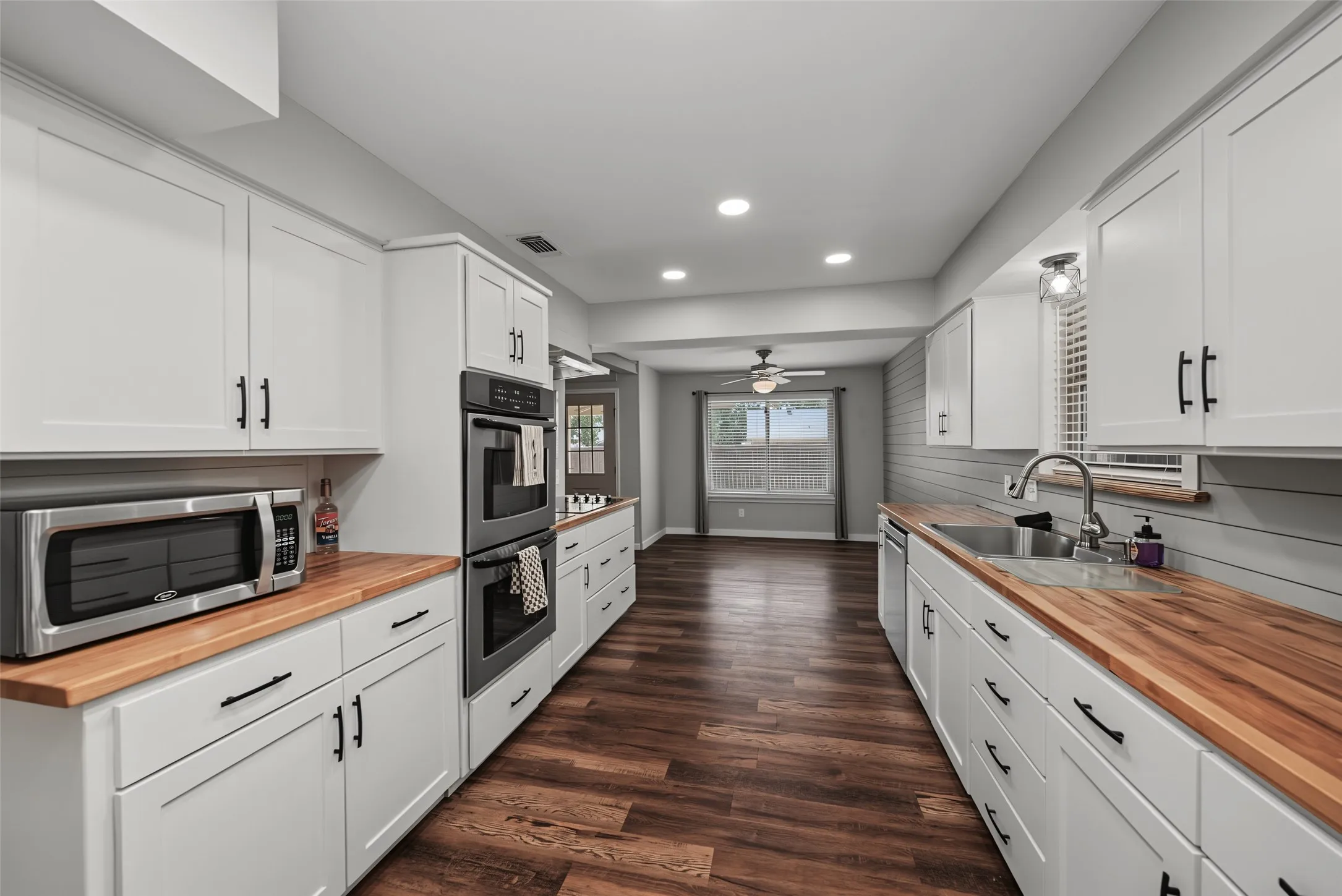 Kitchen featuring white shaker cabinetry, butcher block countertops, stainless steel double ovens, and recessed lighting