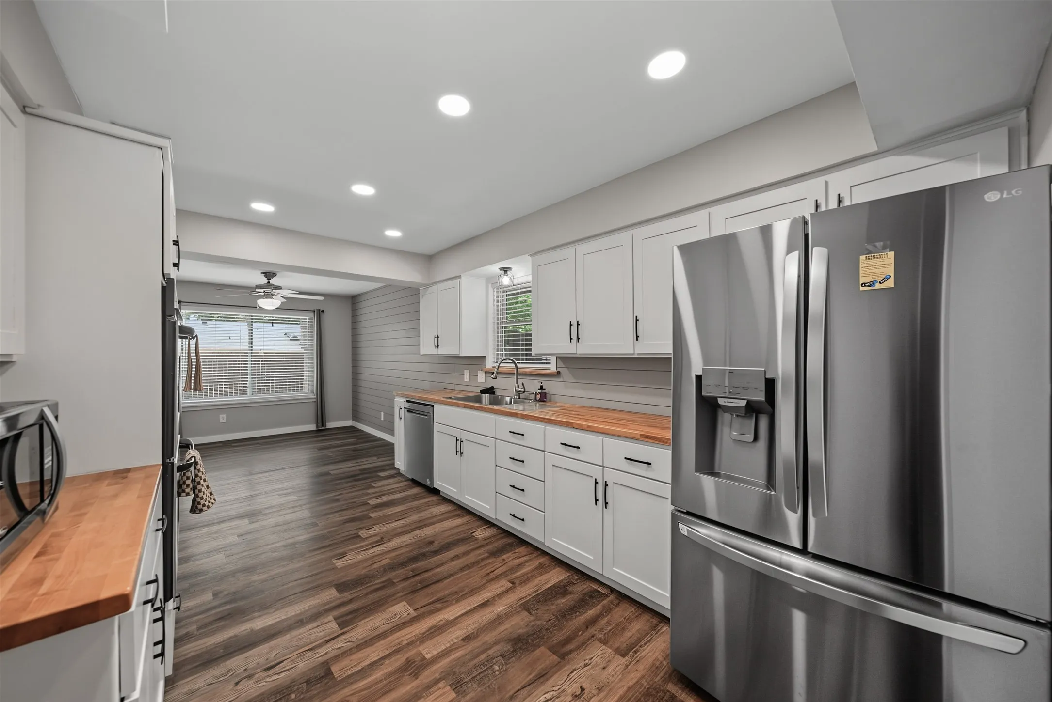 Modern kitchen featuring stainless steel appliances, white cabinetry with dark hardware, butcher block countertops, and recessed lighting