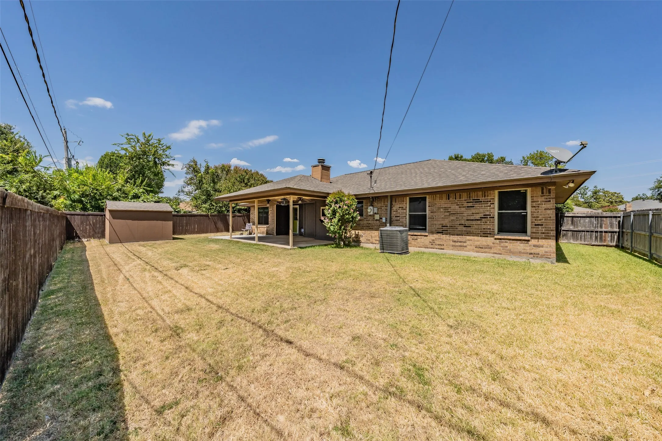 Expansive backyard featuring a covered patio, a detached storage shed, brick exterior, and a privacy fence
