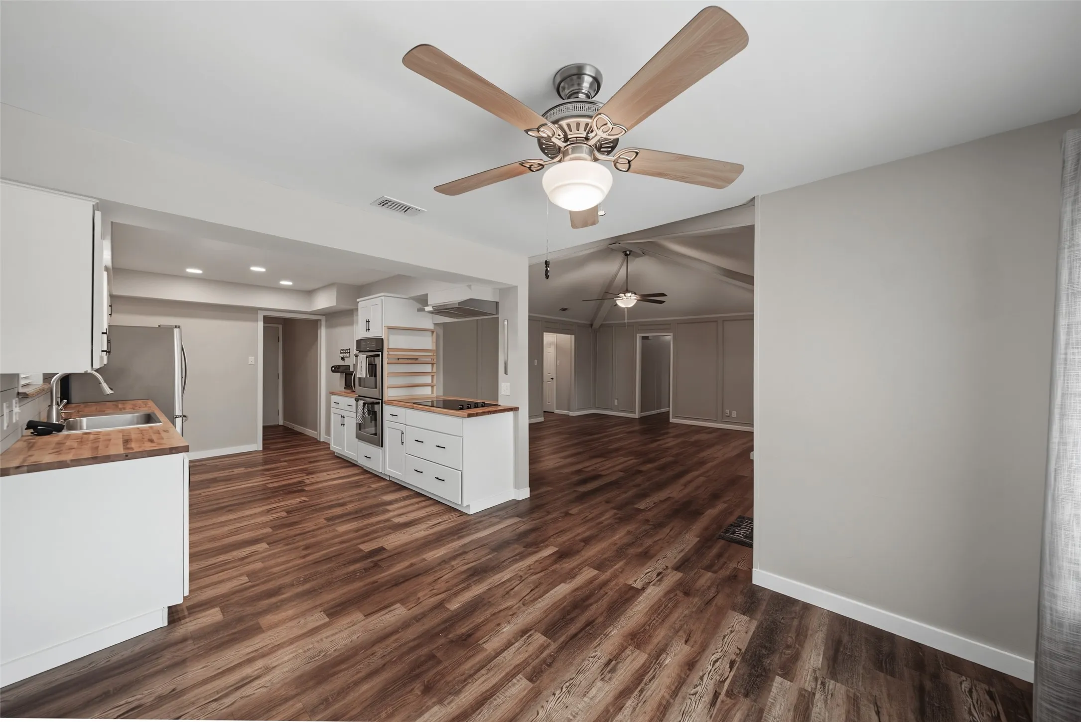 Kitchen featuring luxury vinyl plank flooring, white cabinetry, butcher block countertops, stainless steel refrigerator, and a ceiling fan with integrated lighting