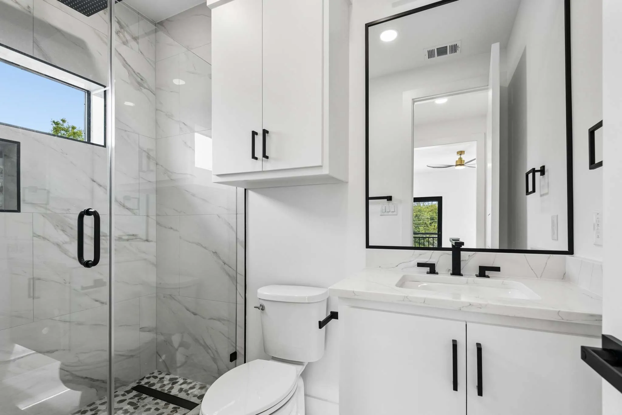 Walk-in shower with glass enclosure, white marble-style tiled walls, and pebble-finish floor