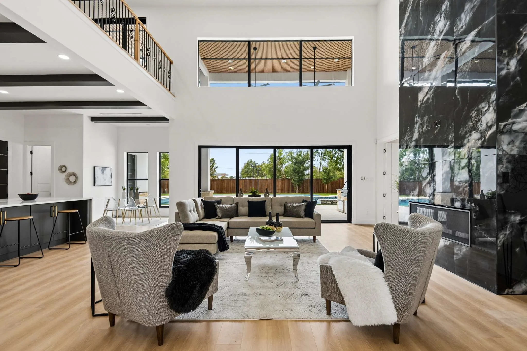 Spacious double-height living area with wood-finish flooring, a large black stone fireplace feature wall, and sliding glass doors to the exterior