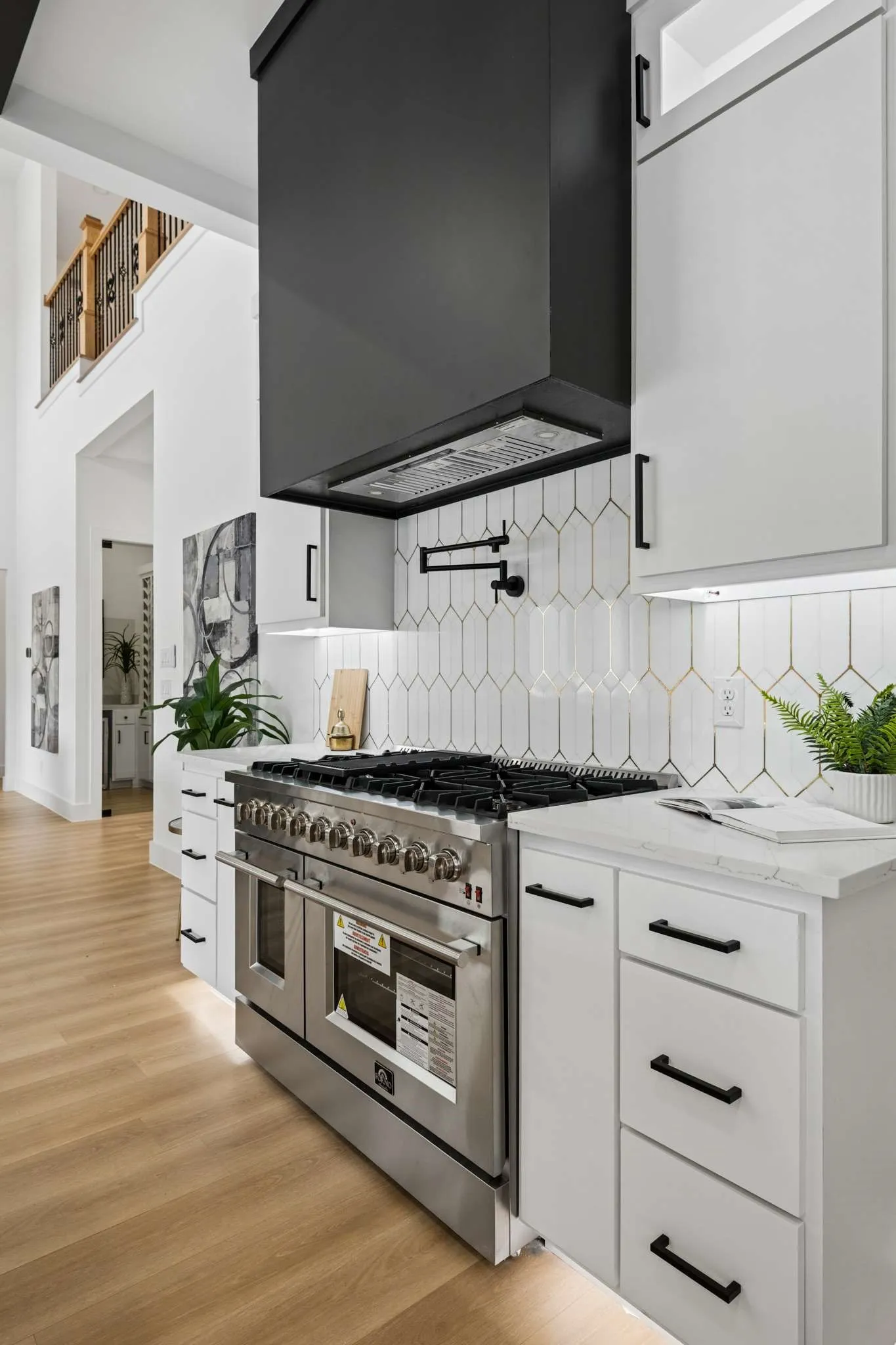 Stainless steel range with a pot filler, matte black range hood, white cabinetry, quartz-finish countertops, and wood-finish flooring