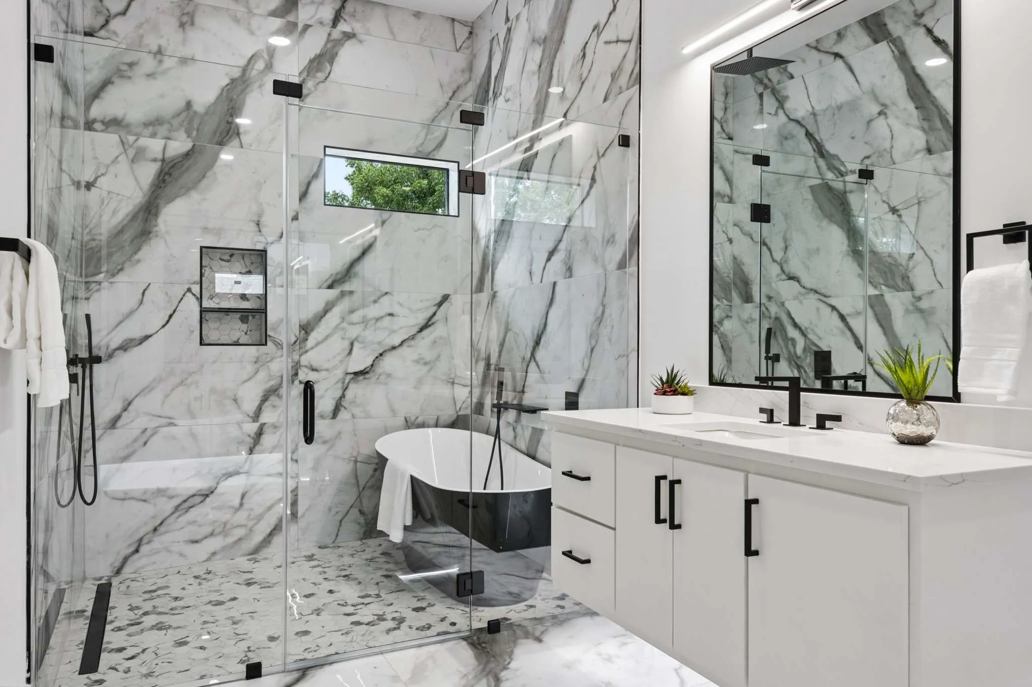 Glass-enclosed shower with full-height stone-look tile walls, integrated shelving, and a built-in bench
