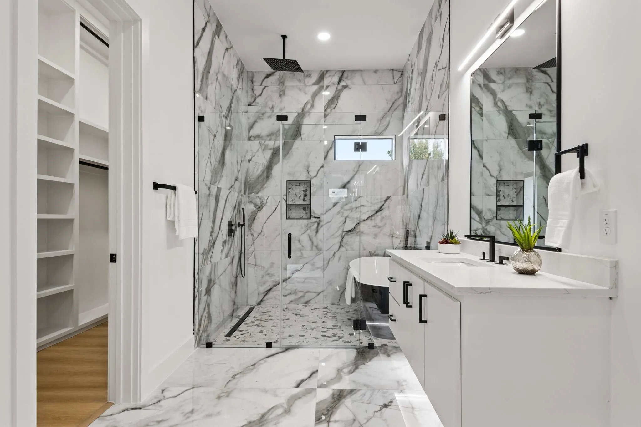 Spacious bathroom featuring a double vanity with stone countertop, large walk-in shower with full-height tile, freestanding tub, and a separate walk-in closet with built-in shelving