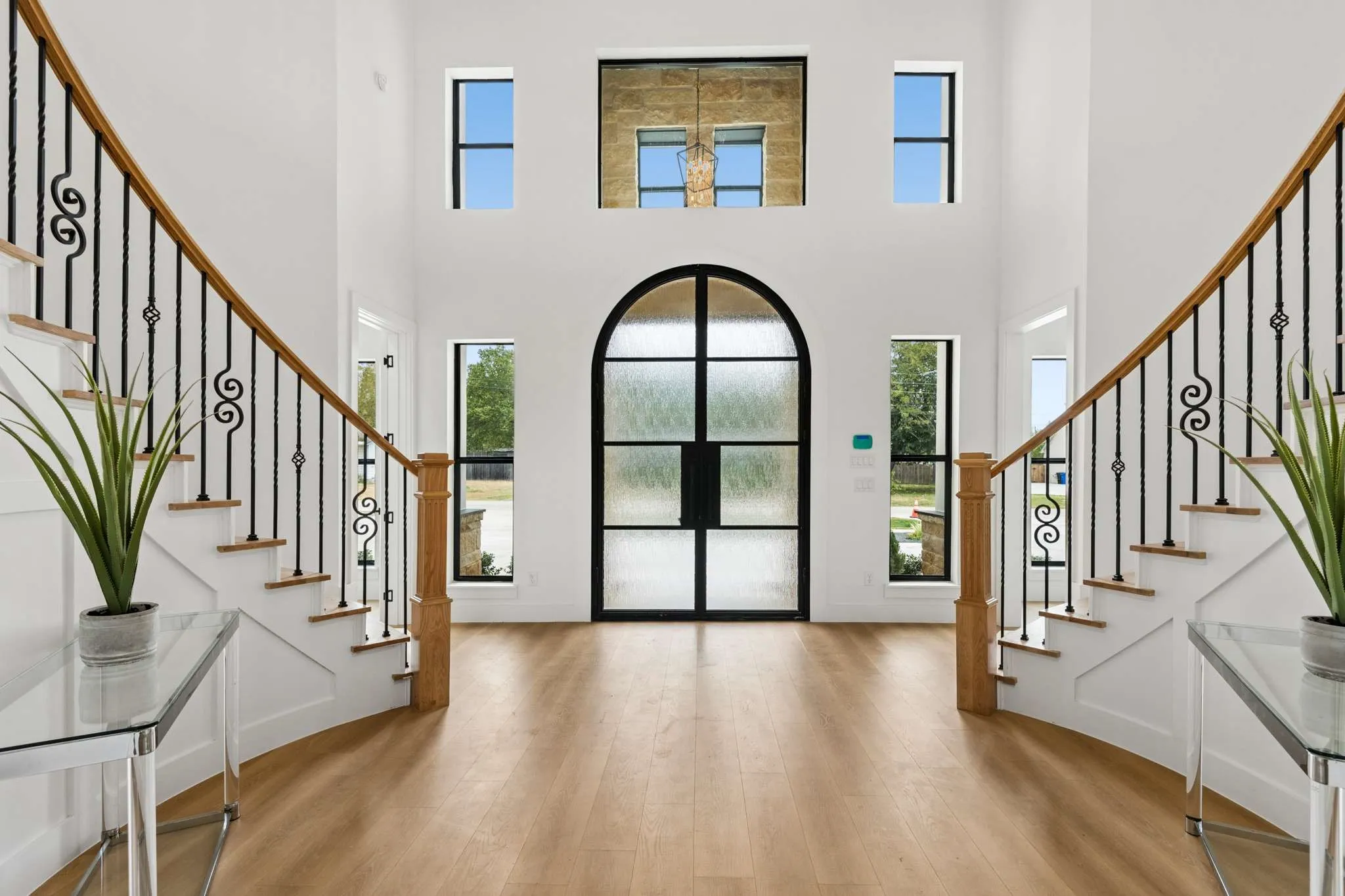 Grand entry with soaring ceilings, a decorative arched entry door with textured glass, wood-finish flooring, and a sweeping staircase with a wood handrail and wrought iron balusters