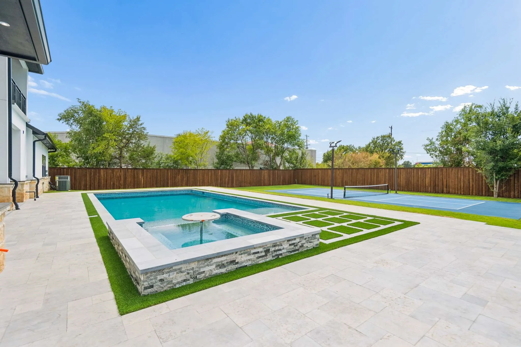 Expansive backyard featuring a rectangular swimming pool, integrated spa, blue hard-surface court, and a wood privacy fence