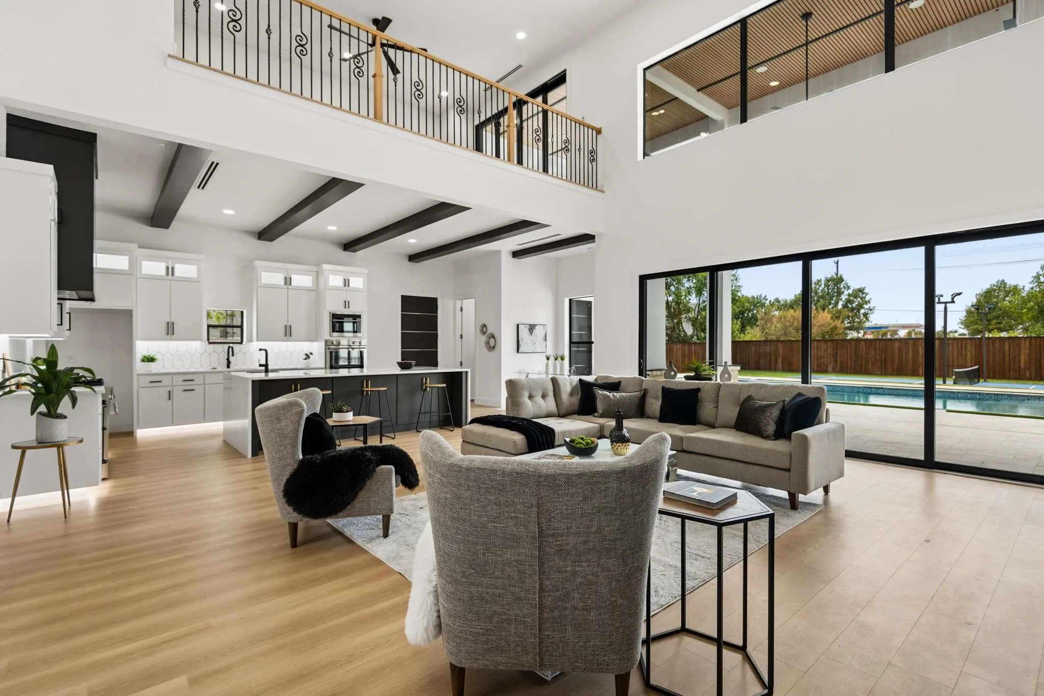 Open-concept living area featuring a two-story ceiling, wood-finish flooring, and a second-level balcony with ornate iron railings