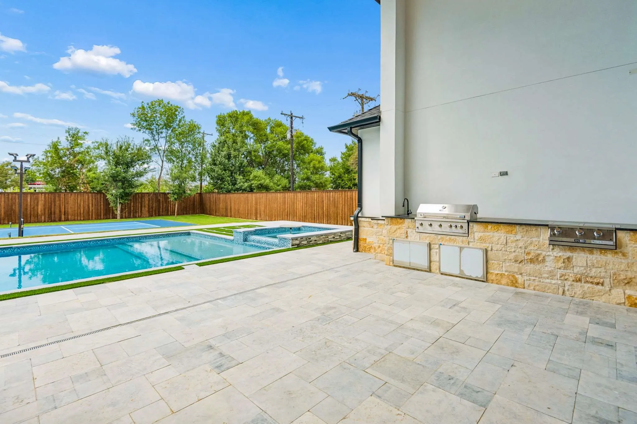 Expansive patio with stone-clad outdoor kitchen featuring a built-in grill and sink