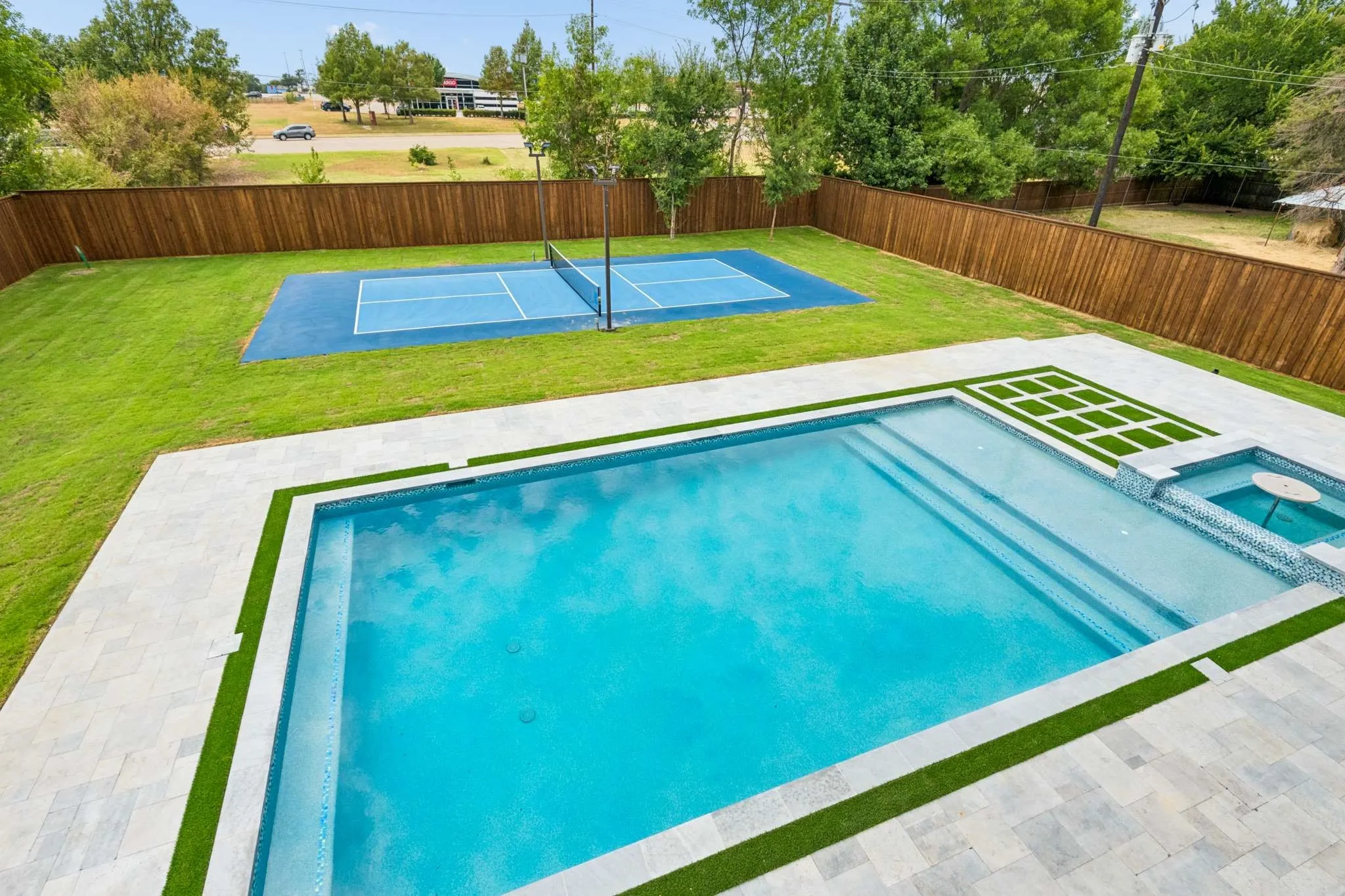 Expansive backyard featuring a rectangular swimming pool with integrated spa, a dedicated sports court, and a privacy fence