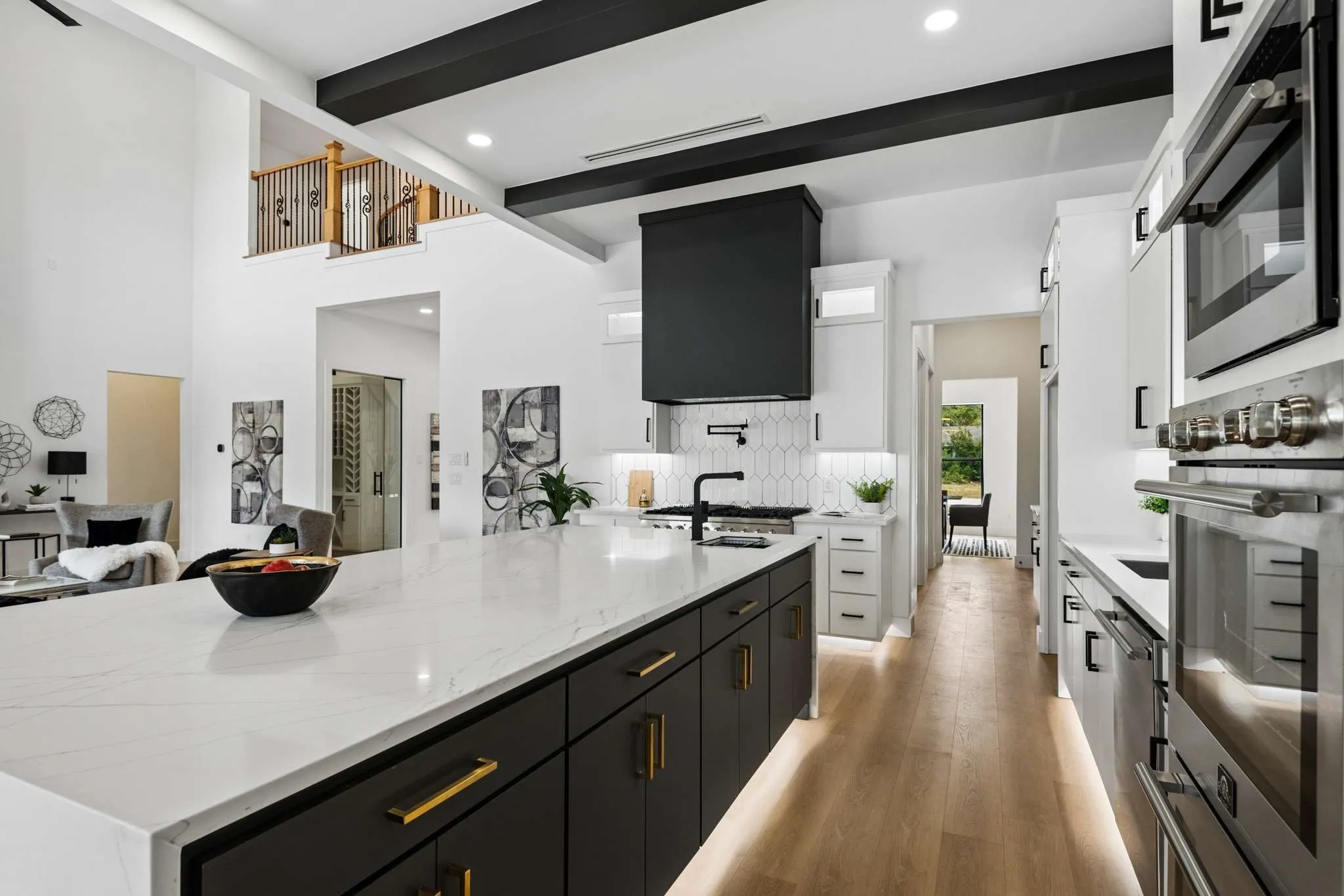 Expansive kitchen featuring a large island with white countertops, stainless steel appliances, wood-finish flooring, and exposed ceiling beams