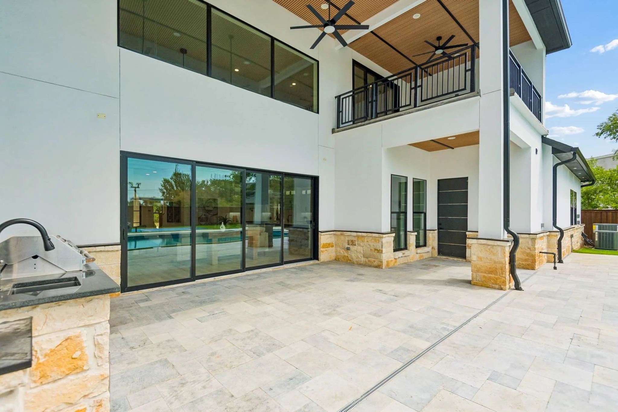 Expansive patio featuring stone tile flooring, an outdoor grilling station with granite countertop, and full-height sliding glass doors