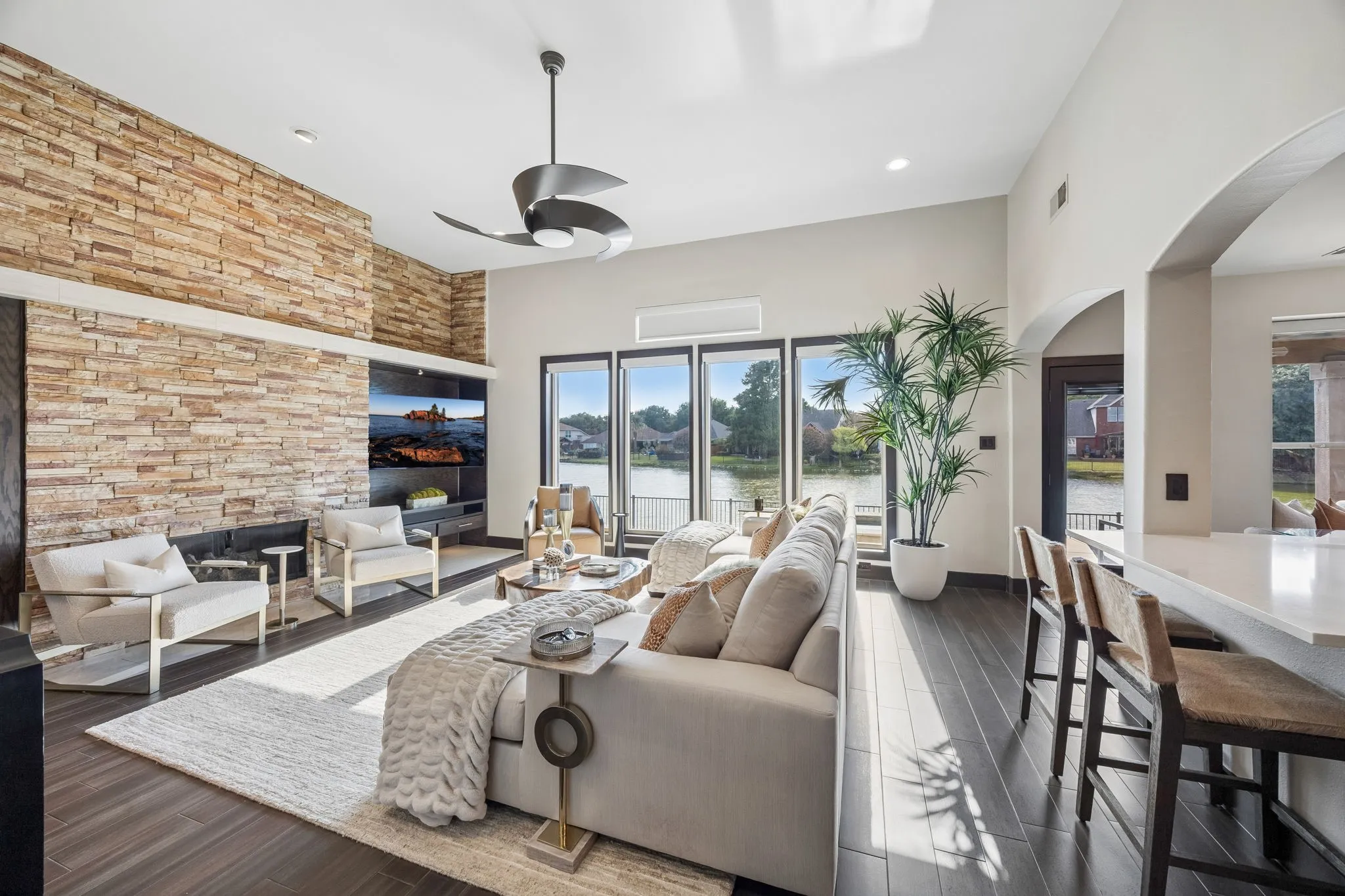 The main living area is anchored by a floor-to-ceiling stone fireplace and walls of windows overlooking the water, creating a seamless connection between the interior and the view beyond.