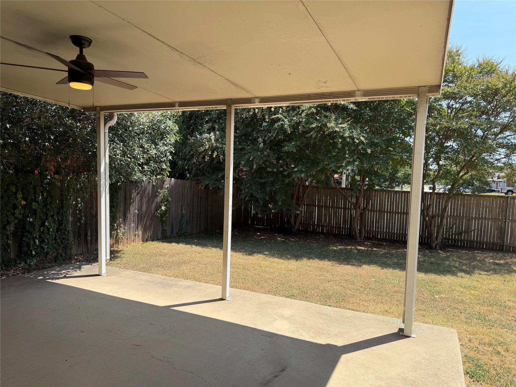 Covered patio featuring a ceiling fan with integrated lighting, concrete surface, and a fenced yard