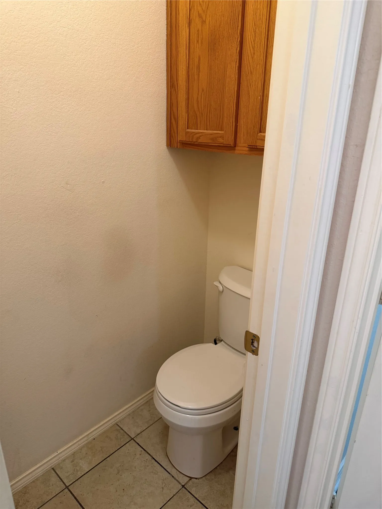 Built-in wood-finish cabinetry, white toilet, and tiled flooring