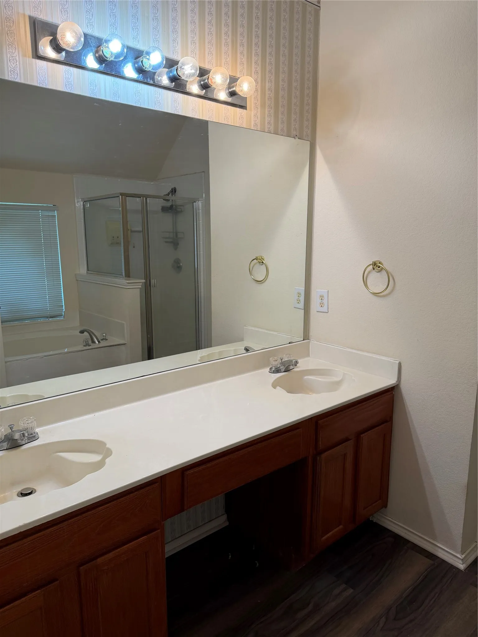 Dual vanity with white countertop, integrated sinks, wood-finish cabinetry, and a large wall mirror