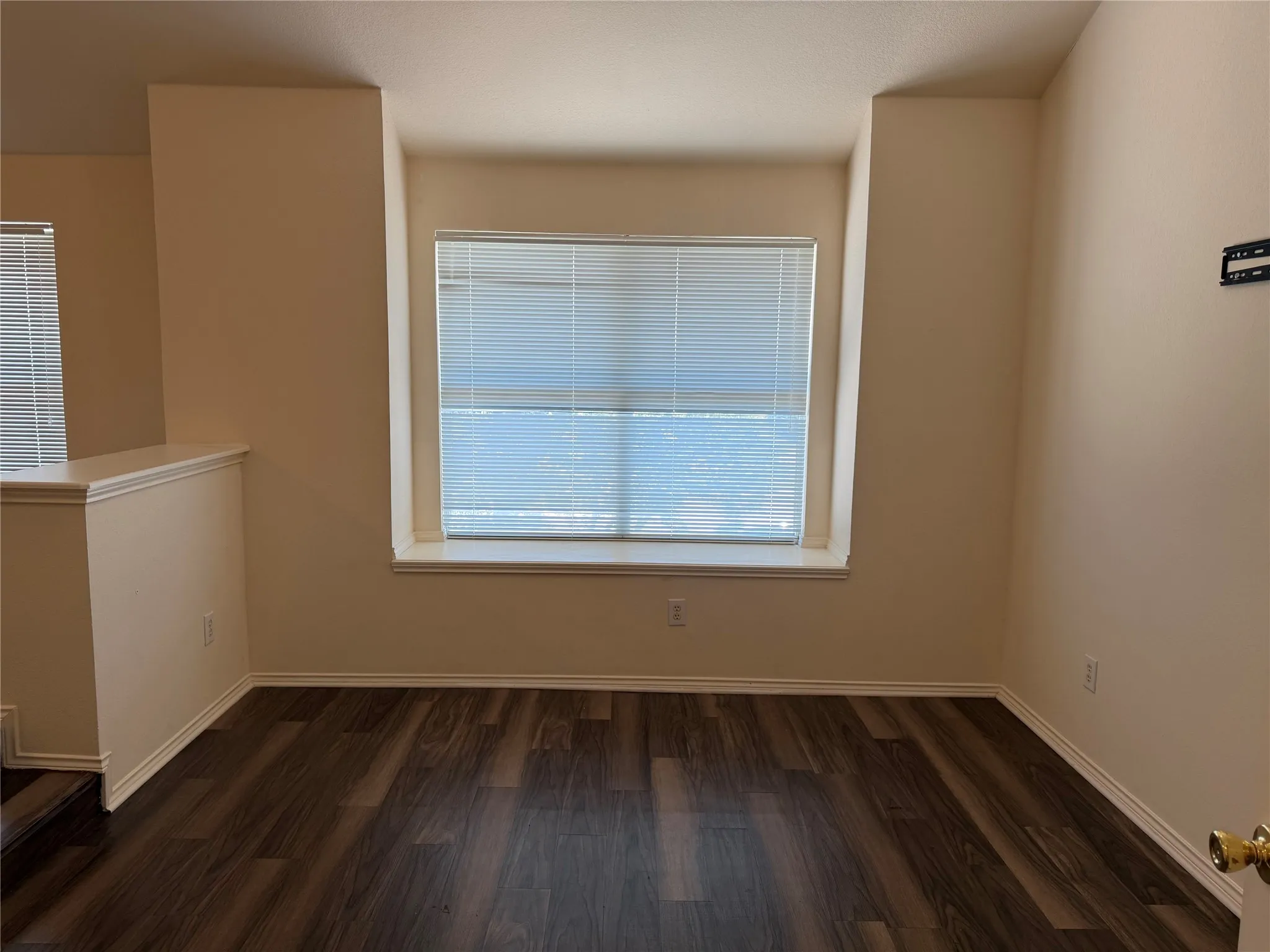 Spacious room featuring wood-finish flooring, neutral paint, and ample natural light through a large window
