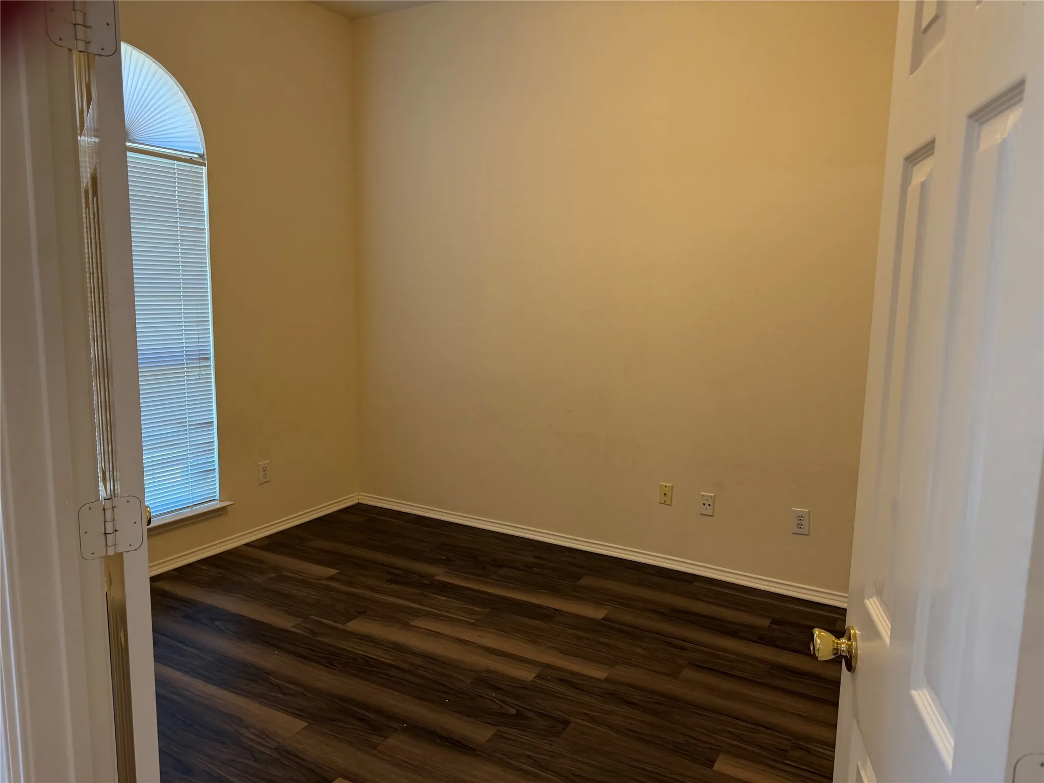 Room featuring wood-finish flooring, a tall arched window with blinds, and neutral wall tones