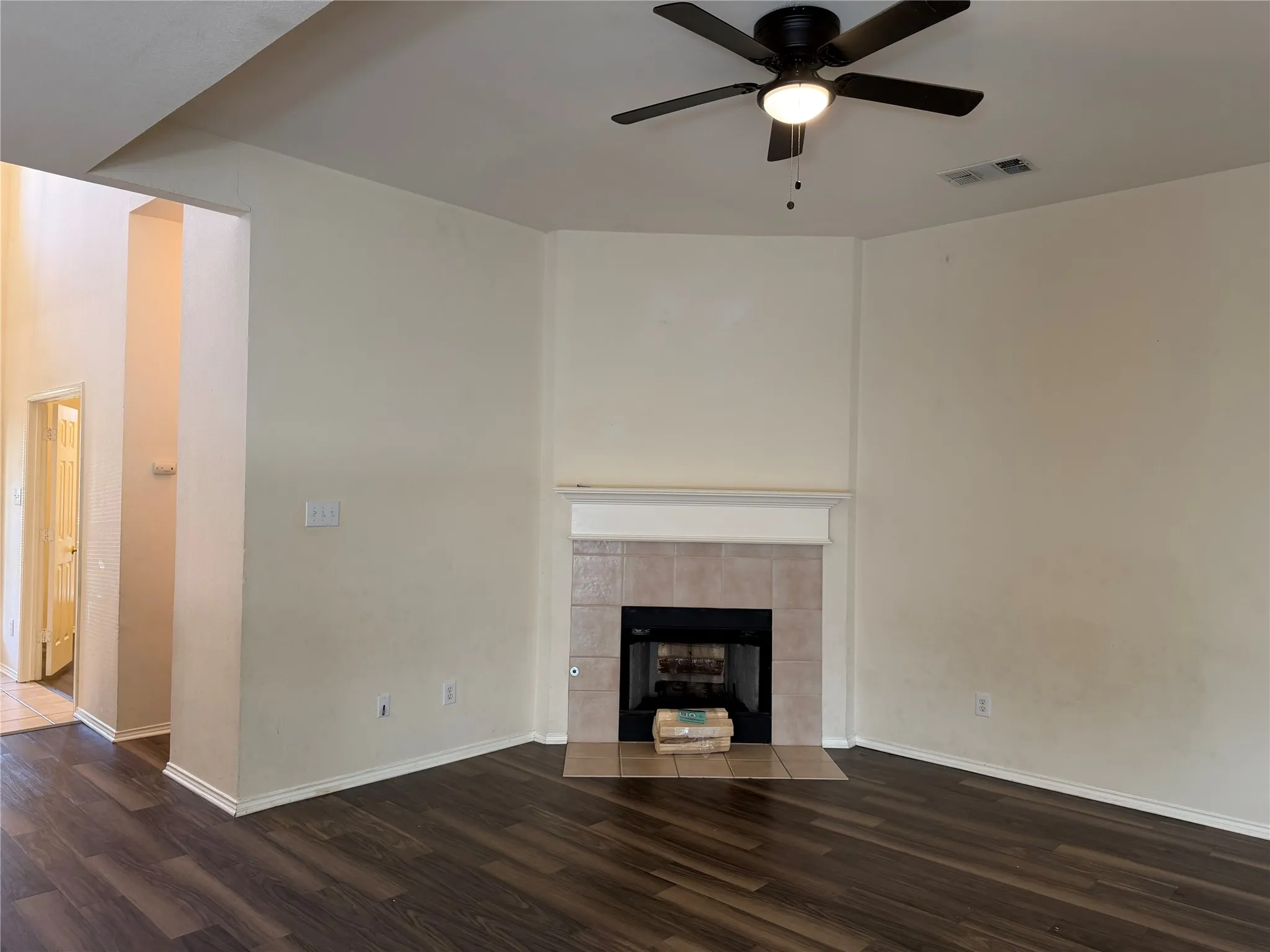 Wood-finish flooring throughout, tile-surround fireplace with mantel, and a ceiling fan with integrated lighting