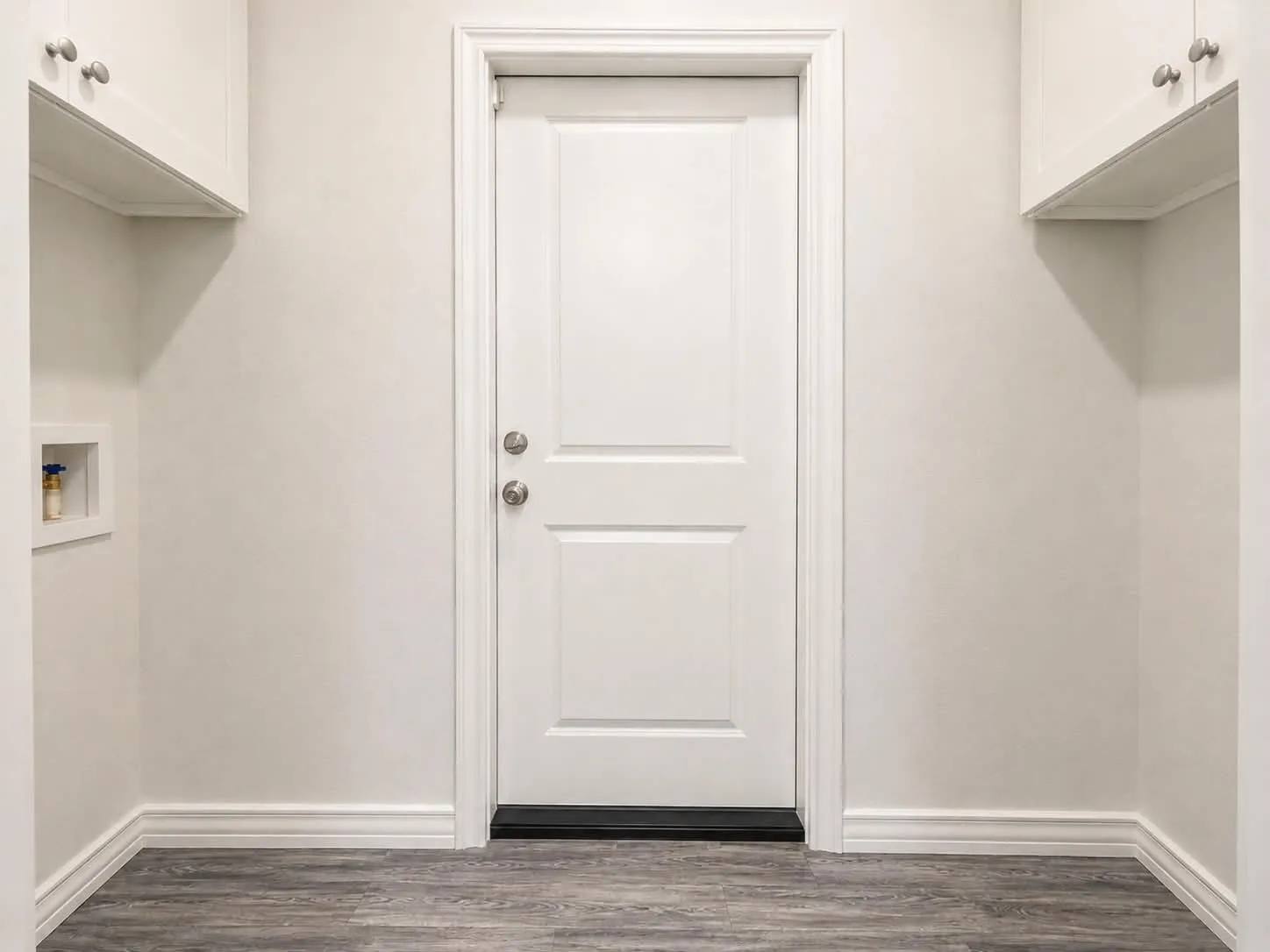 White paneled door with brushed nickel hardware, white upper cabinetry with chrome knobs, and wood-finish flooring