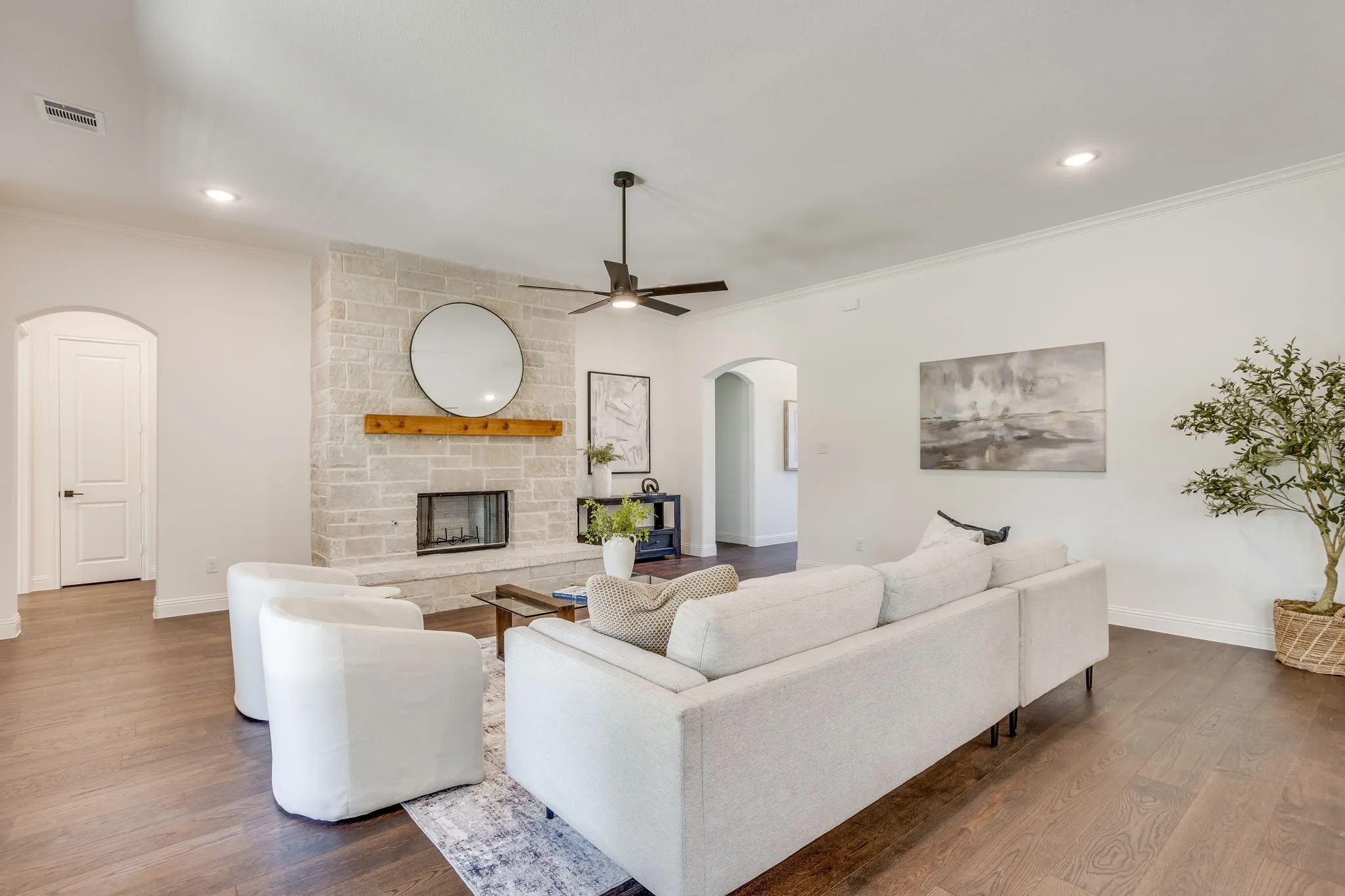 Stone-clad fireplace with a wood mantel, wood-finish flooring, recessed lighting, ceiling fan, and arched doorways