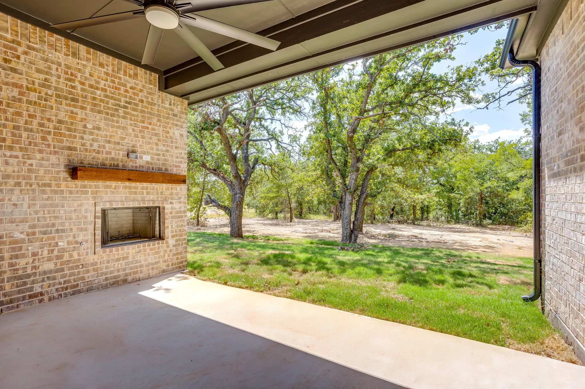 Covered patio with brick-finish wall, built-in fireplace, and cedar mantel