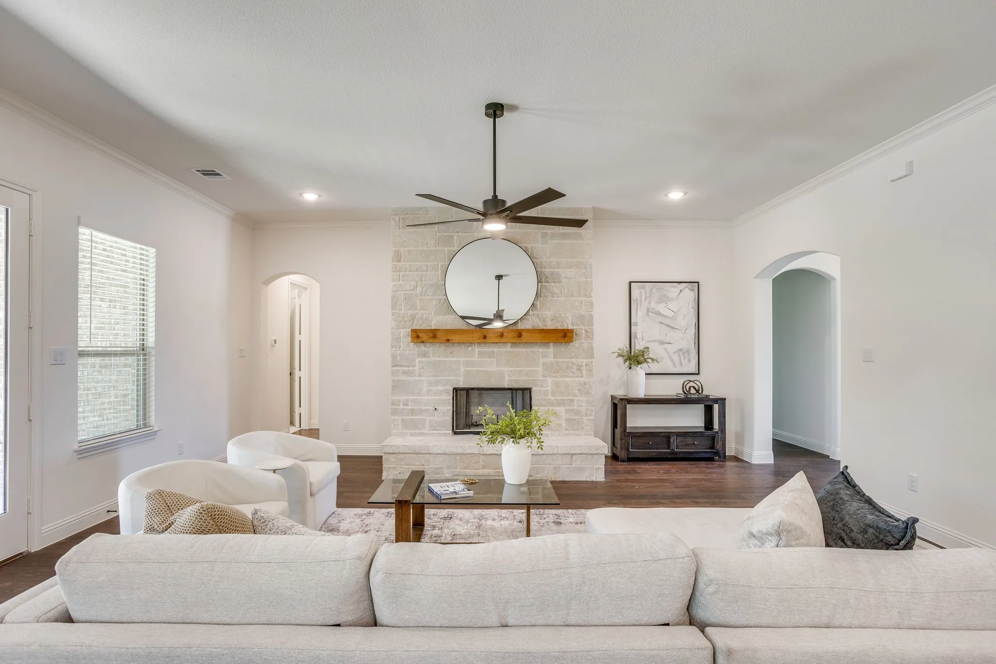 Stone-clad fireplace with a wood mantle, ceiling fan with integrated lighting, recessed lighting, arched entryways, and wood-finish flooring