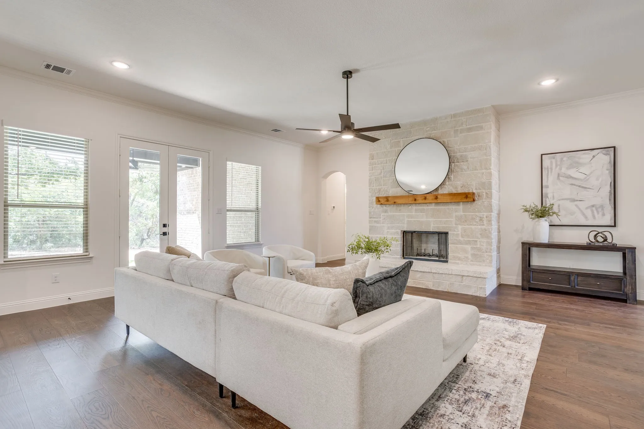 Stone-clad fireplace with wood mantel, dark wood-finish flooring, recessed lighting, ceiling fan, and French doors