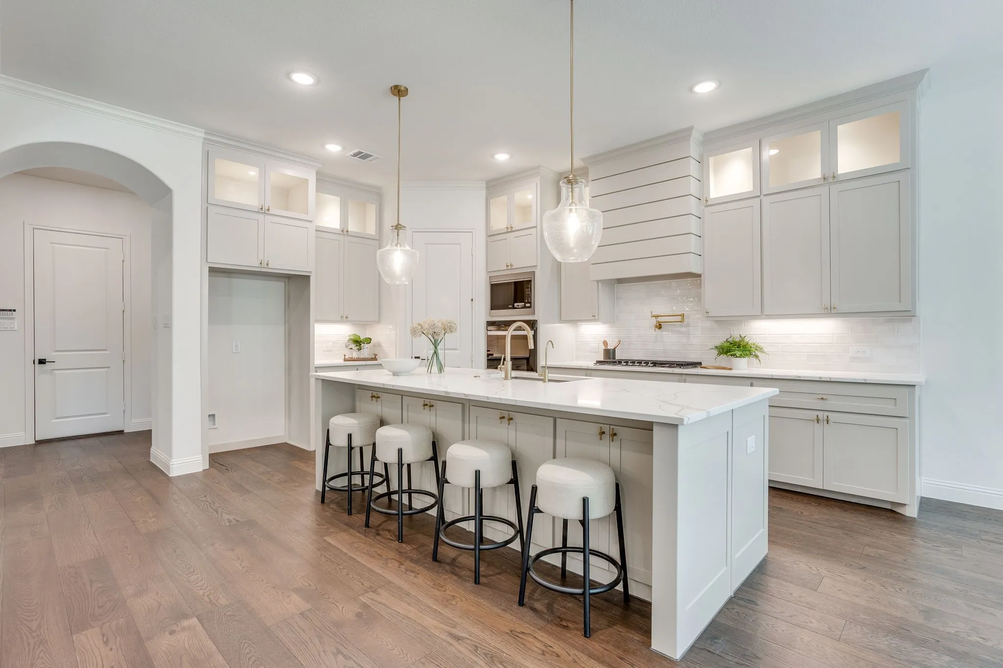 Spacious kitchen featuring a large central island, white cabinetry, integrated appliances, wood-finish flooring, and pendant lighting