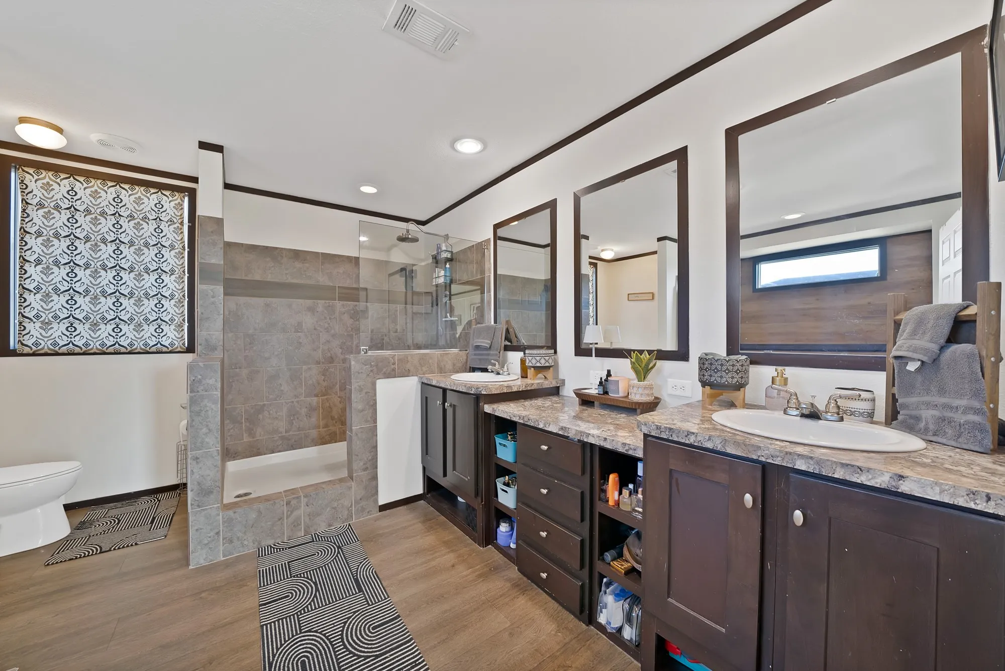 Dual vanity with integrated sinks and dark cabinetry, large tiled walk-in shower with glass enclosure, wood-finish flooring, and recessed lighting