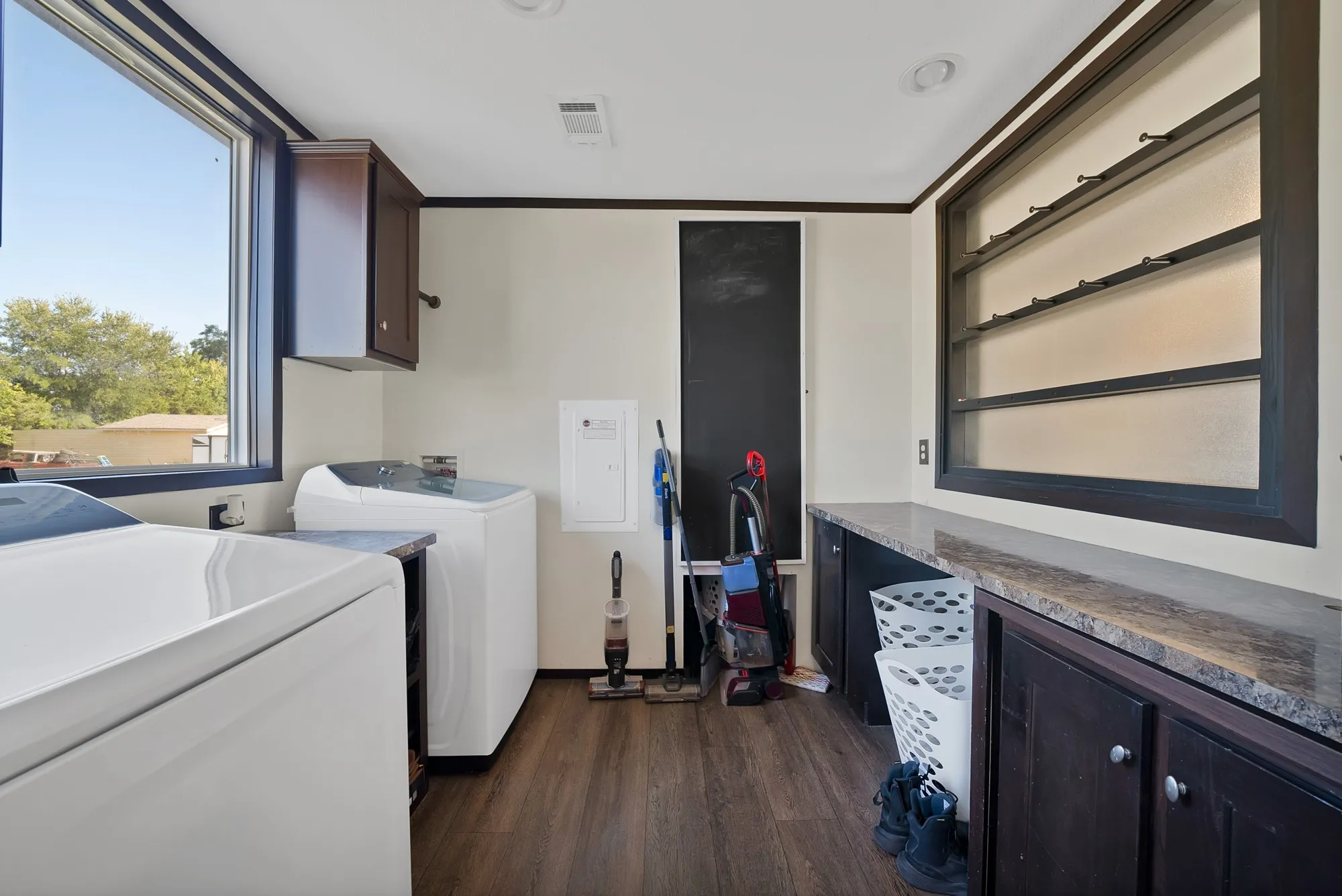 Spacious utility room featuring wood-finish flooring, a large window, dark wood cabinetry with a light-colored countertop, and a built-in shelving unit