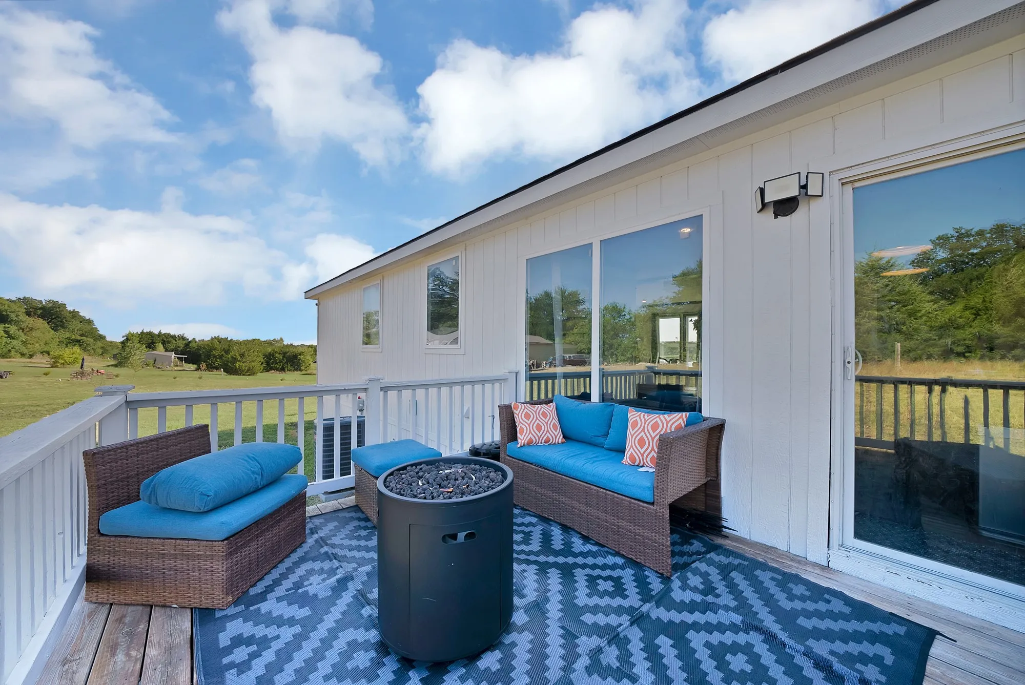 Exterior wood deck featuring a white railing, sliding glass doors, white siding, and a prominent sky backdrop