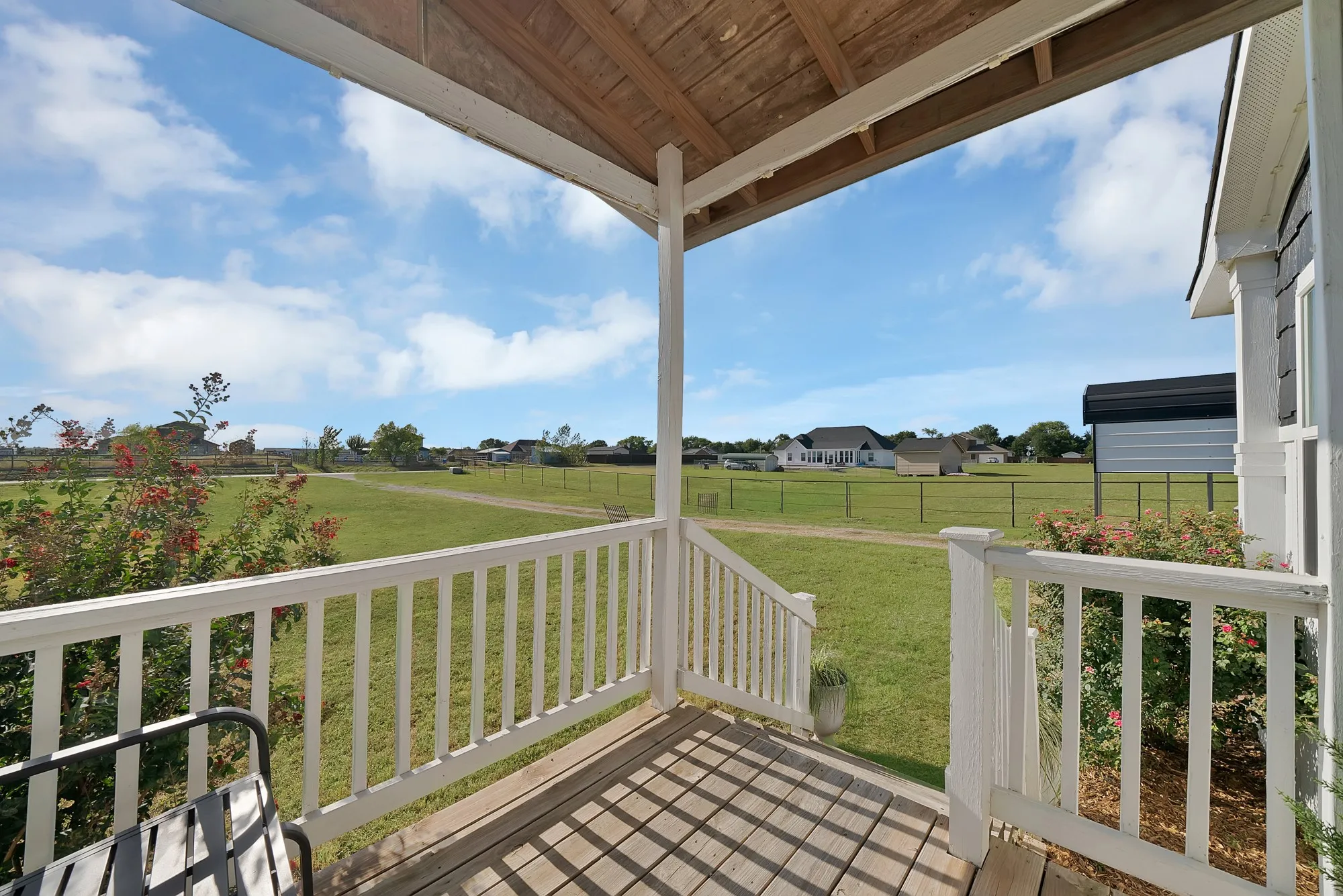 Covered porch with wood ceiling and flooring, white railings, and expansive green landscape