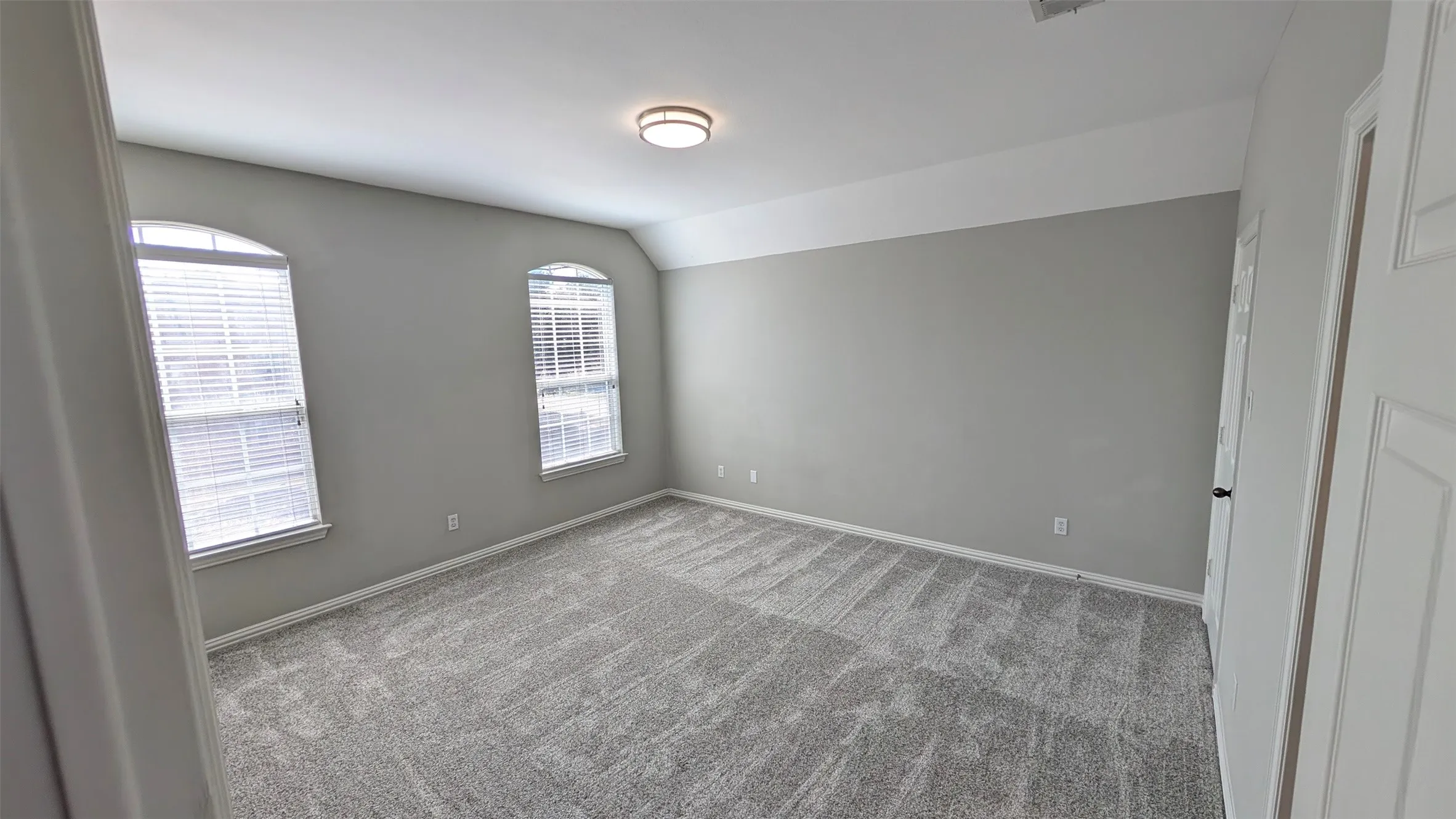 Carpeted room with neutral wall paint, two arched windows featuring blinds, and a flush mount ceiling light