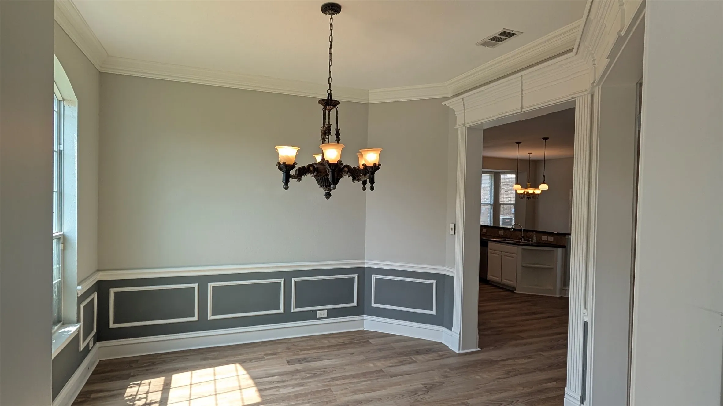 Vaulted ceiling, wood-finish flooring, wainscoting, decorative trim, and an ornate chandelier