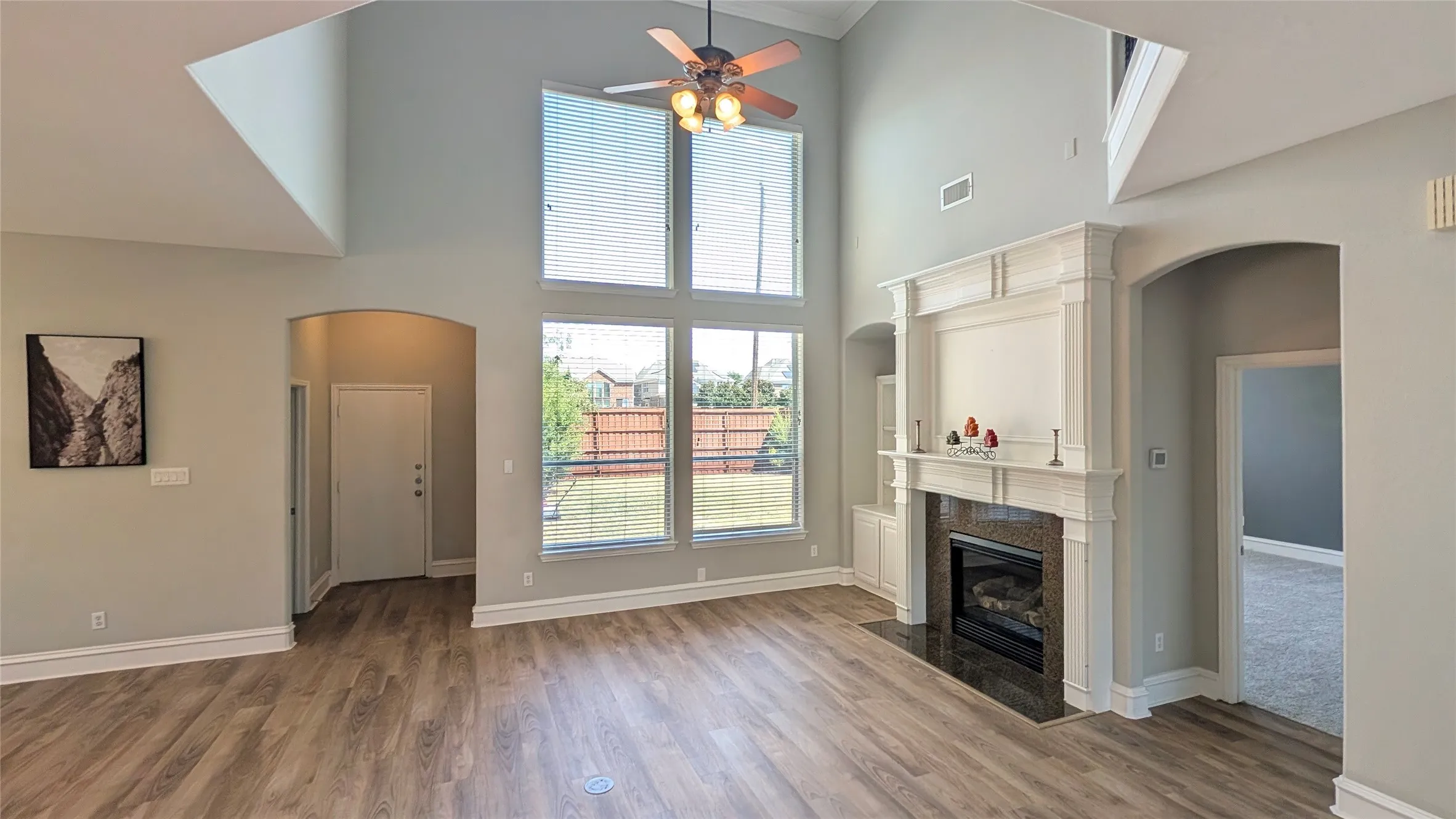 Vaulted ceiling with a ceiling fan, fireplace with a decorative mantel and dark stone surround, wood-finish flooring, and large windows