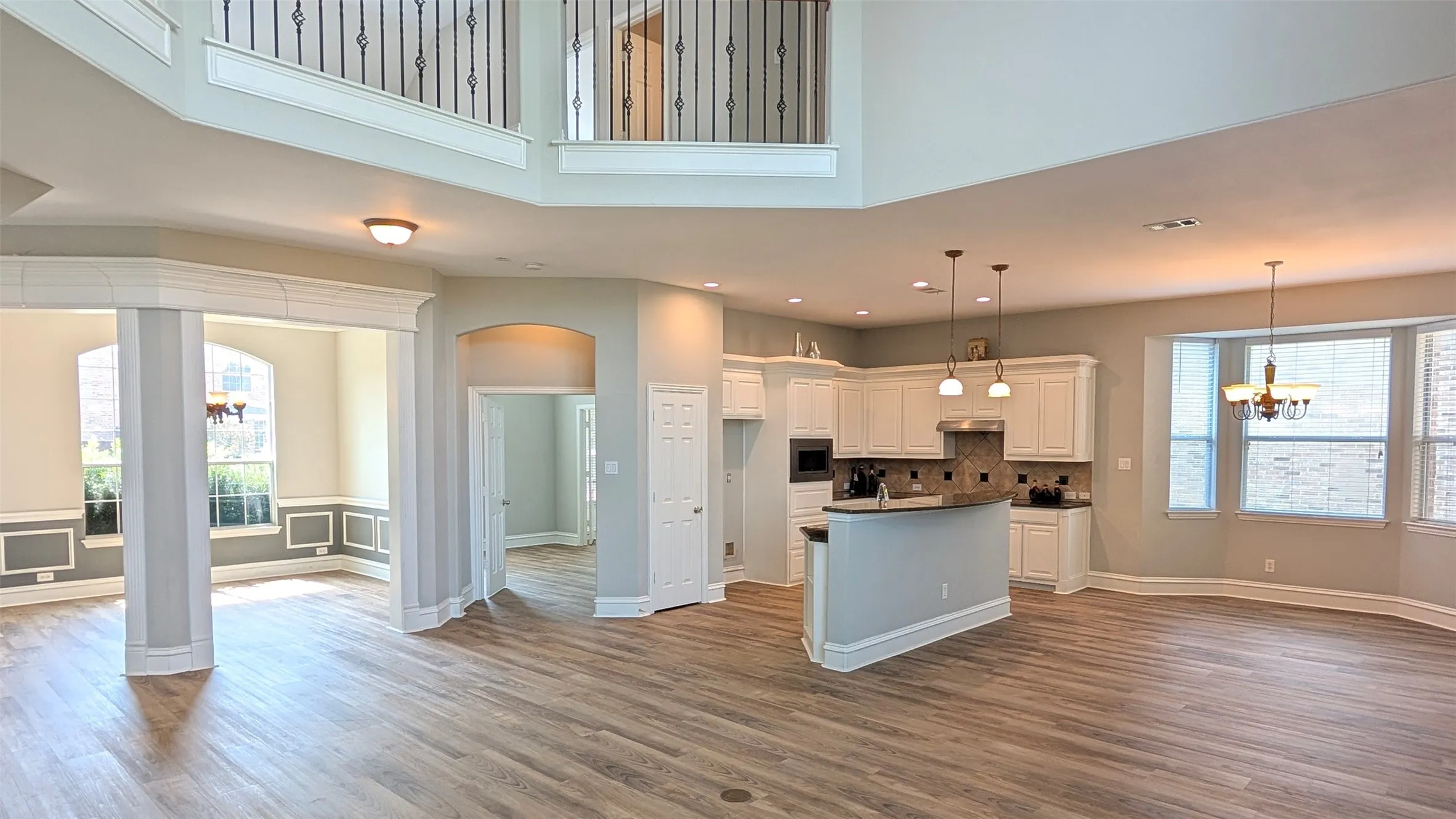 Open-concept living area with wood-finish flooring, a two-story ceiling, and a kitchen featuring white cabinetry and an island