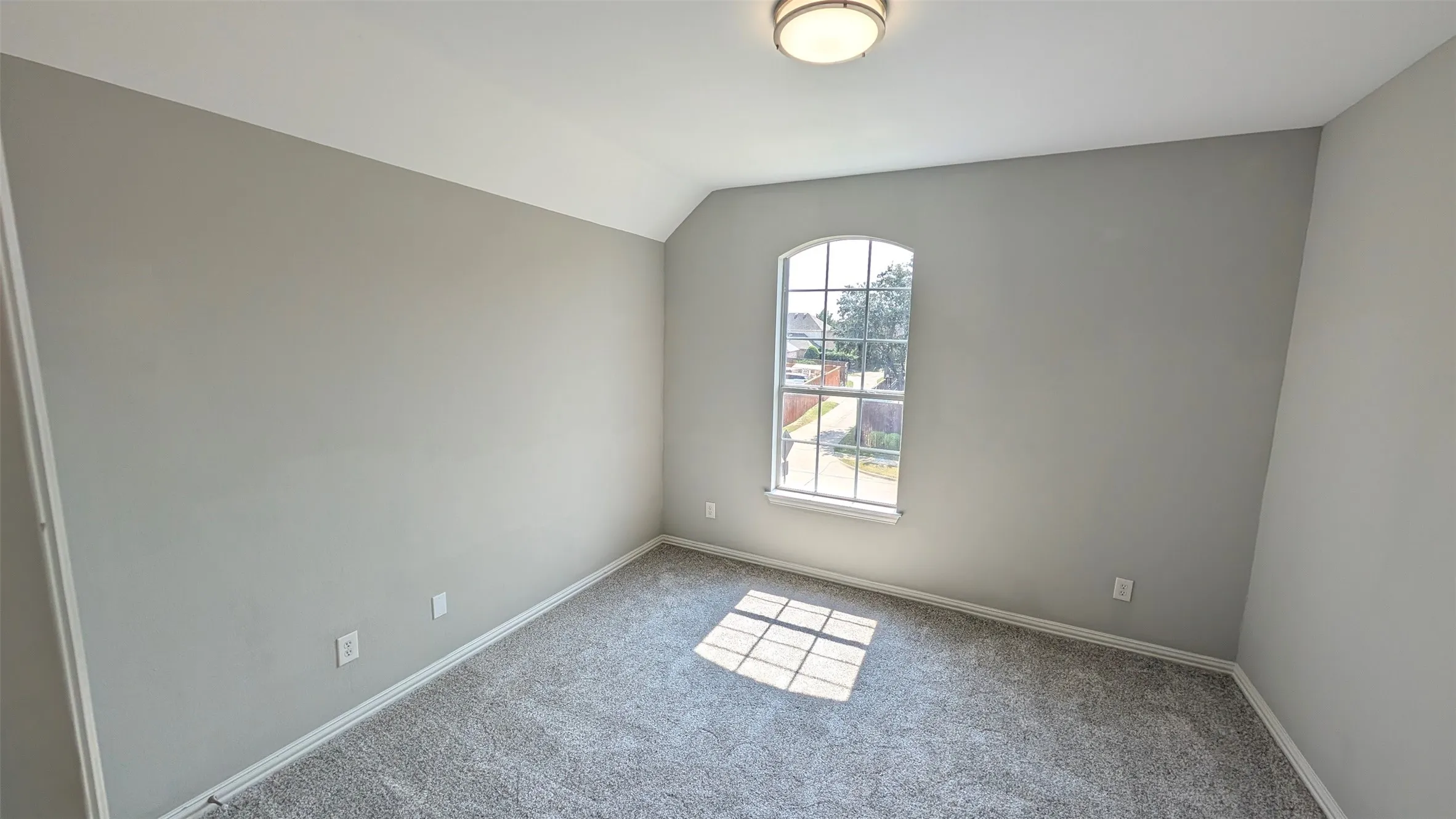 Neutral tone walls, grey carpeting, arched window, and a flush-mount ceiling light