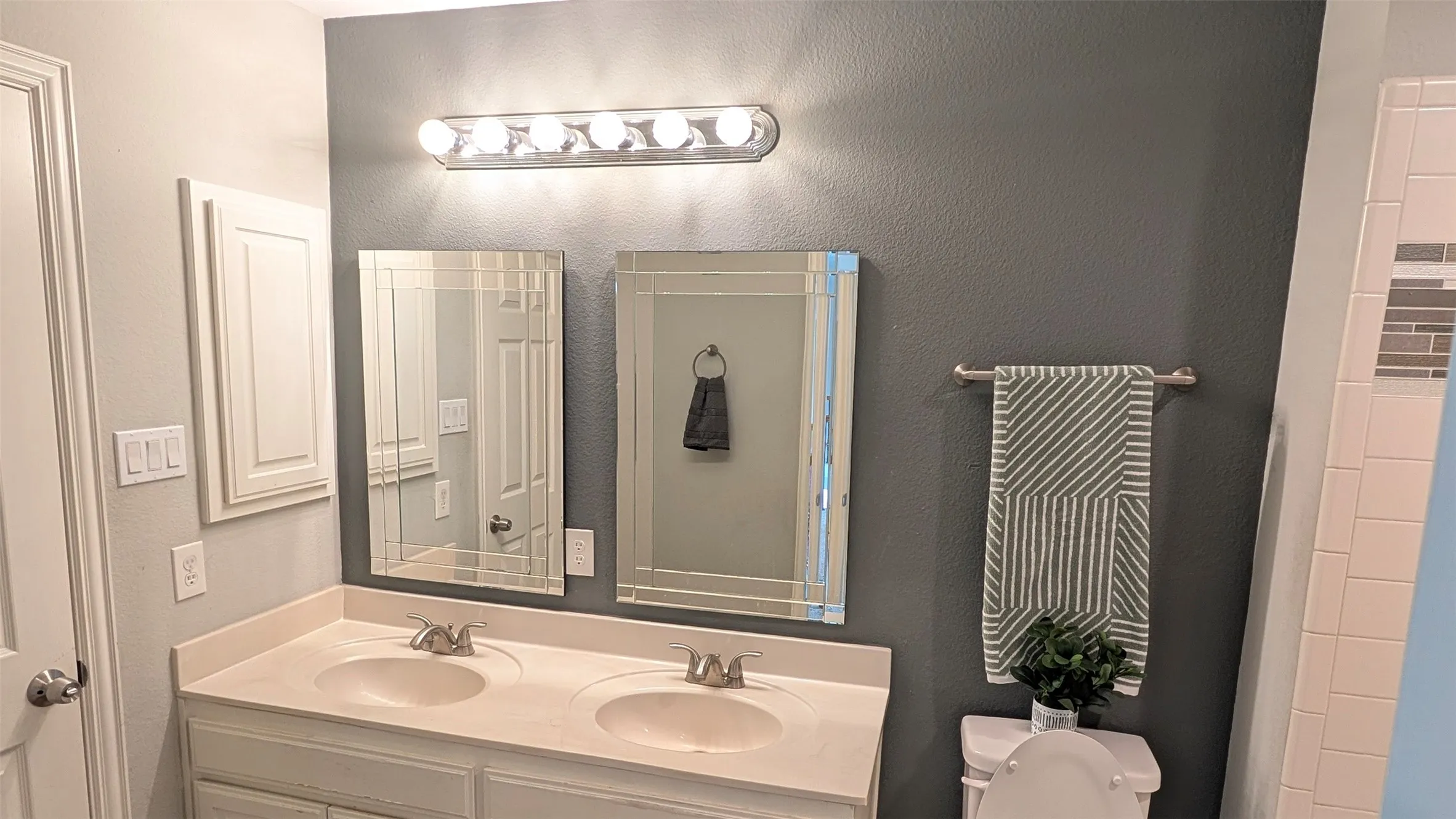 Dual vanity with integrated sinks, framed mirrors, wall-mounted light fixture, and built-in medicine cabinet