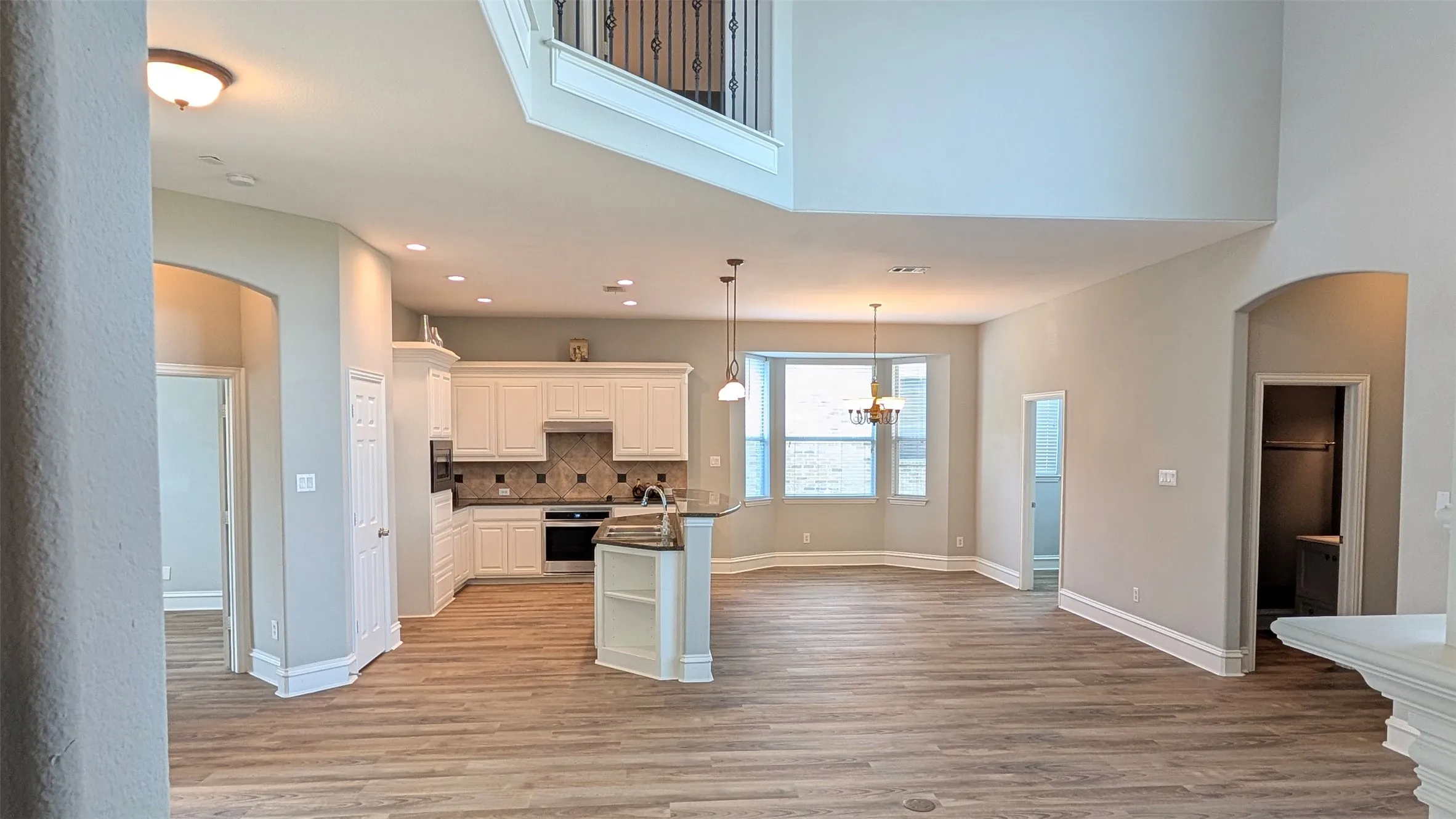 Open-concept living area featuring wood-finish flooring, a kitchen island with built-in shelving, white cabinetry, and recessed lighting