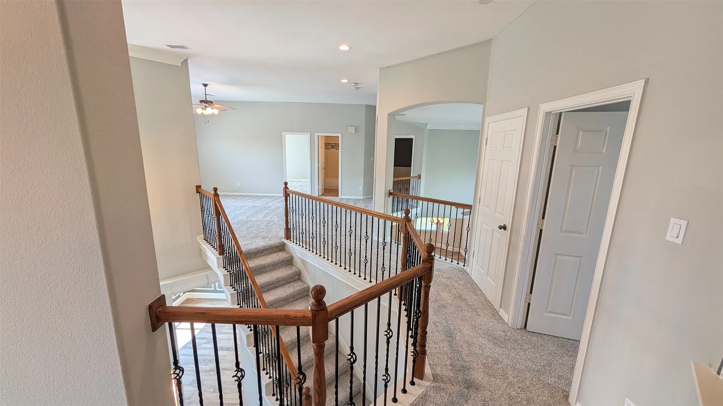 Elegant second-floor landing featuring a wood-finish staircase with metal spindle railing, recessed ceiling lighting, and neutral carpeting throughout