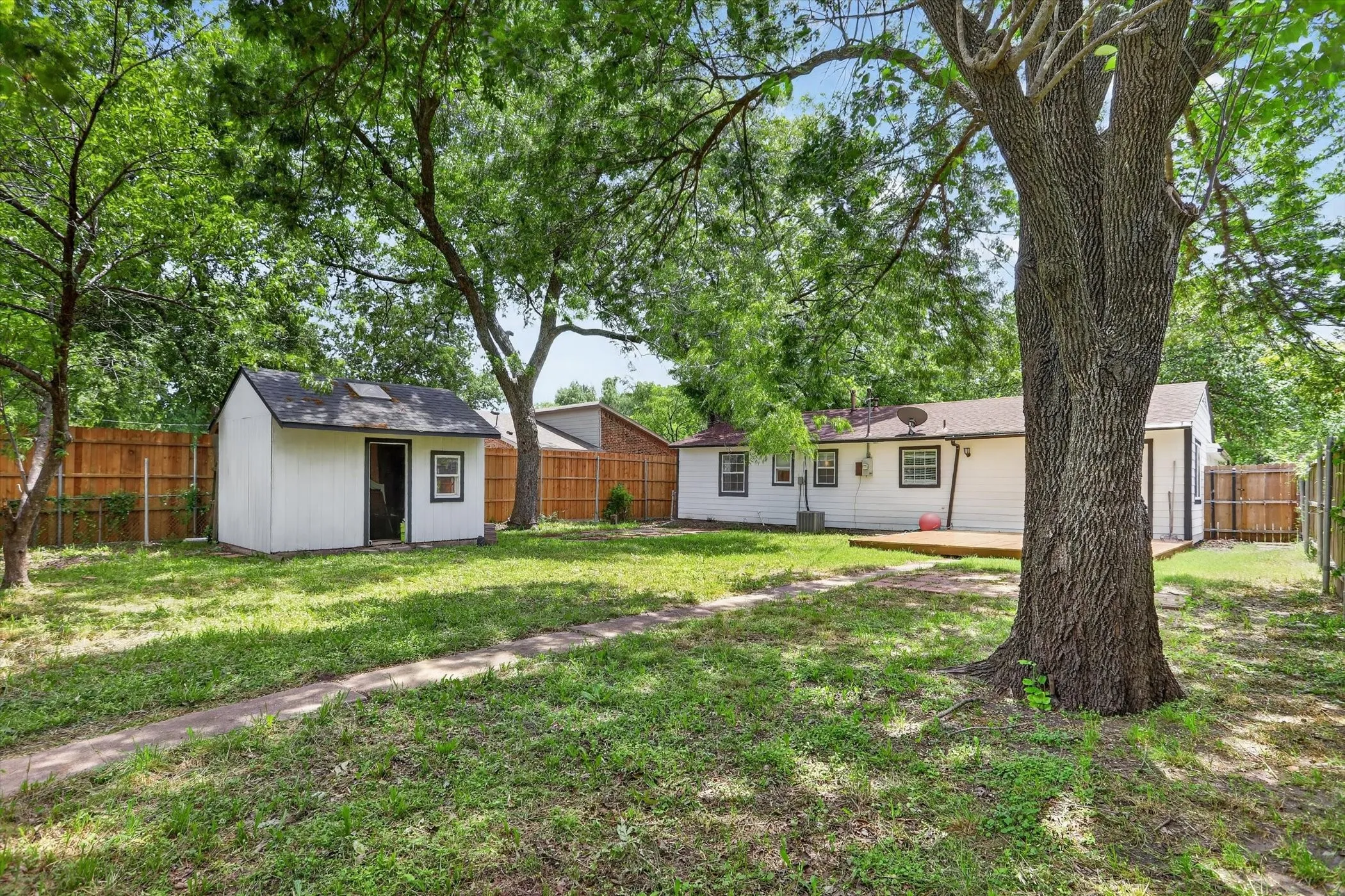 Expansive backyard with a manicured lawn, established trees, and a wooden privacy fence