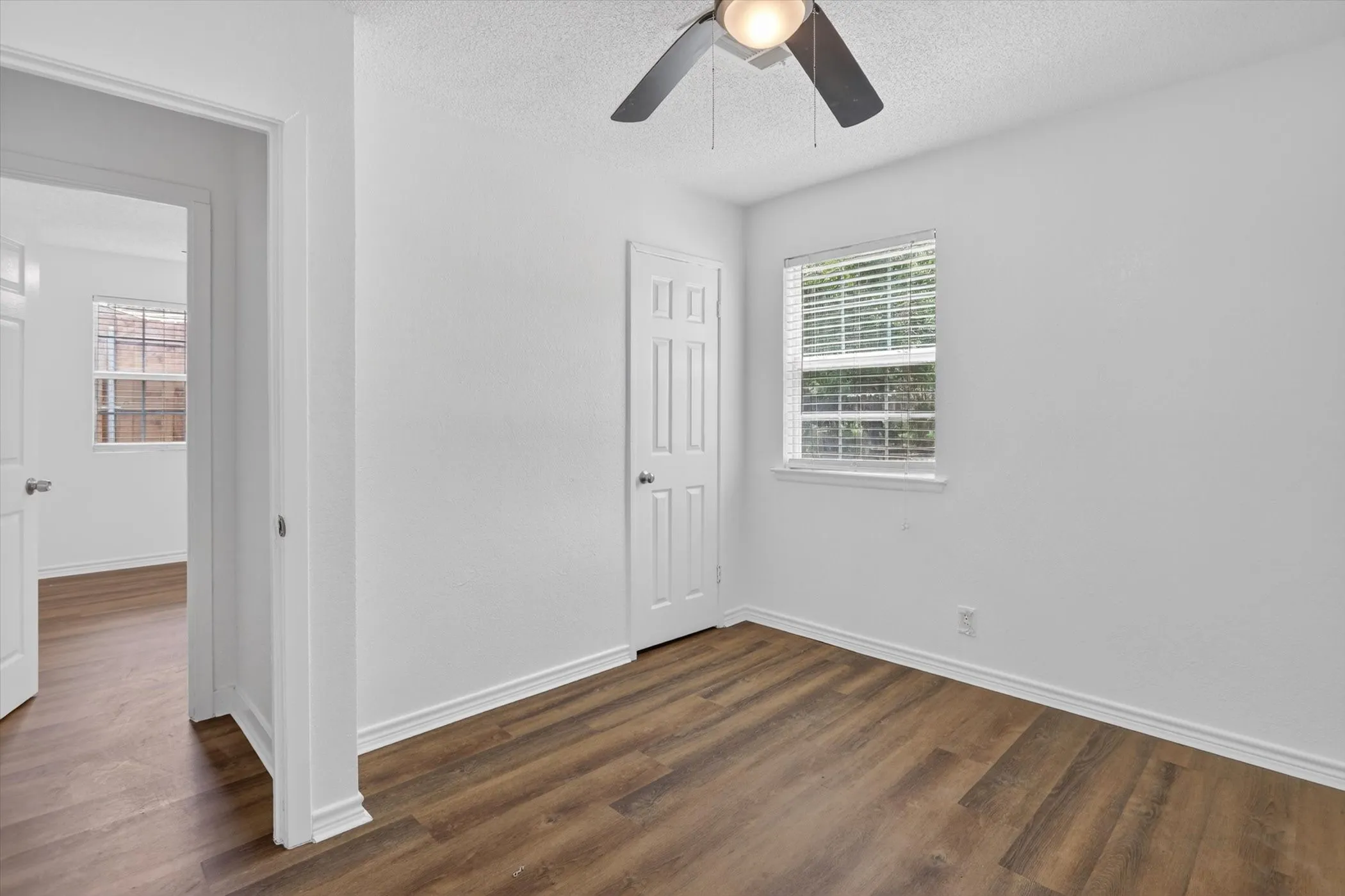 Room featuring wood-finish flooring, white walls, and a ceiling fan with integrated lighting