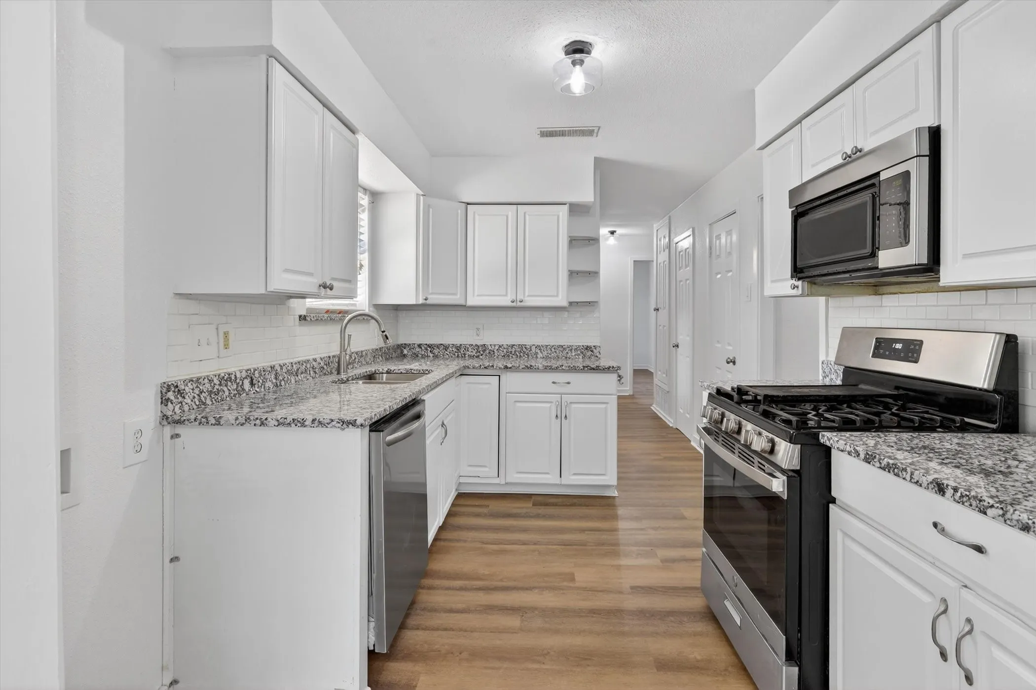 Contemporary kitchen featuring white cabinetry, granite-style countertops, stainless steel appliances, a subway tile backsplash, and wood-finish flooring