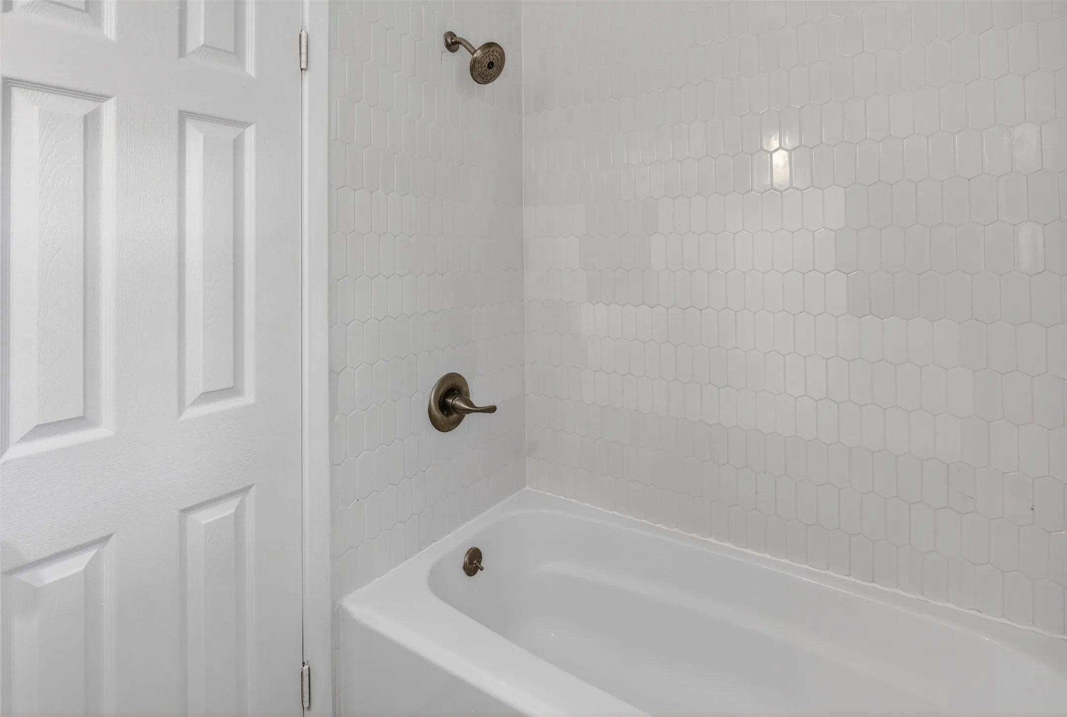 Bathtub and shower combination featuring a white tiled surround with a picket pattern